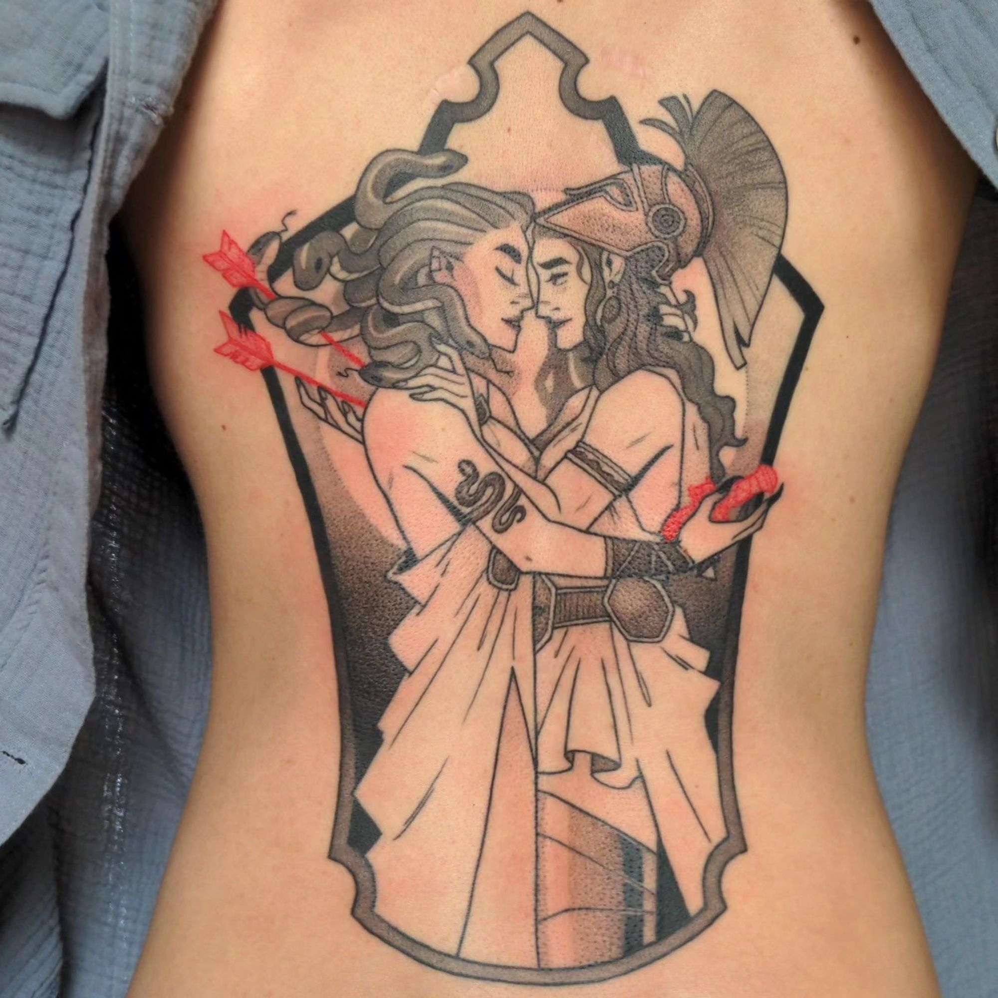 A full back (mostly) black and grey tattoo of Medusa and Athena in a loving embrace. They are both cradling the red weapons in each other's backs. they look serene, with their heads together.