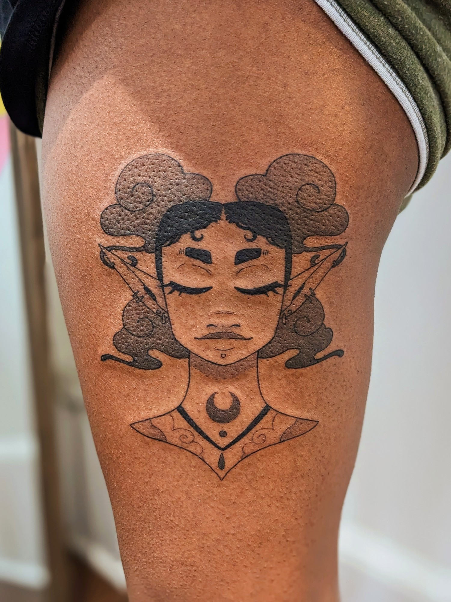 A black and grey symmetrical portrait tattoo of a bkack air genasi elf. She has a neutral, happy expression with closed eyes. Her curly hair, done up in four space buns, transforms into wisps of smoke.