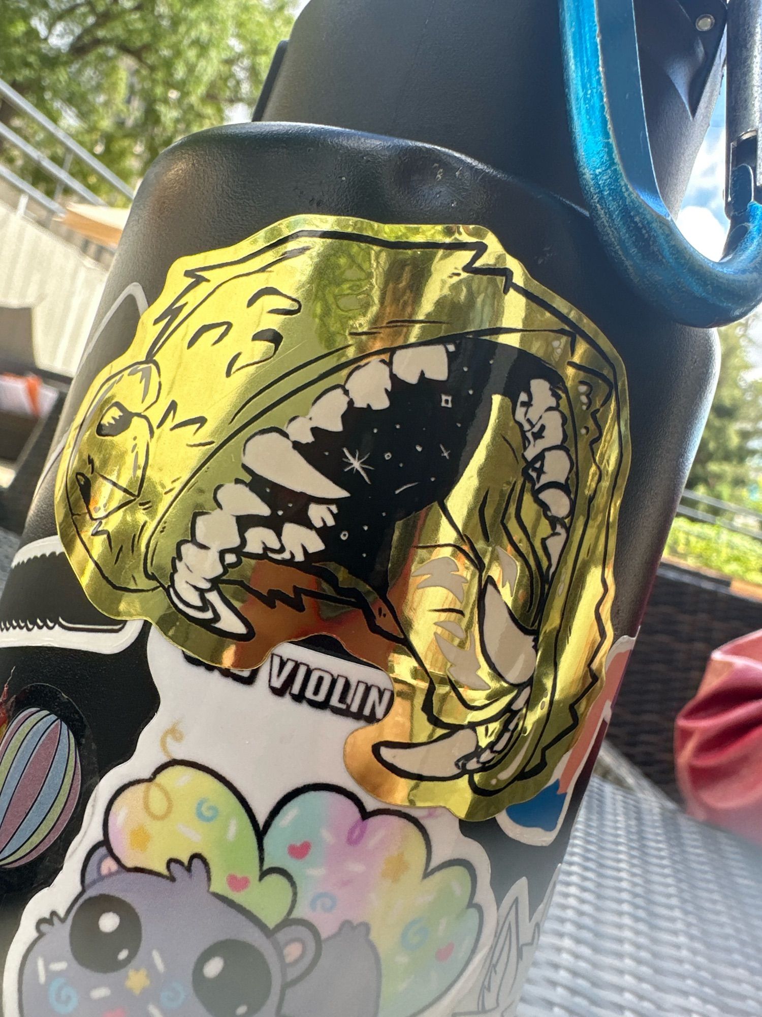 Pictured a water bottle with stickers all over it, focusing on the golden sticker of a mean looking open wolf maw