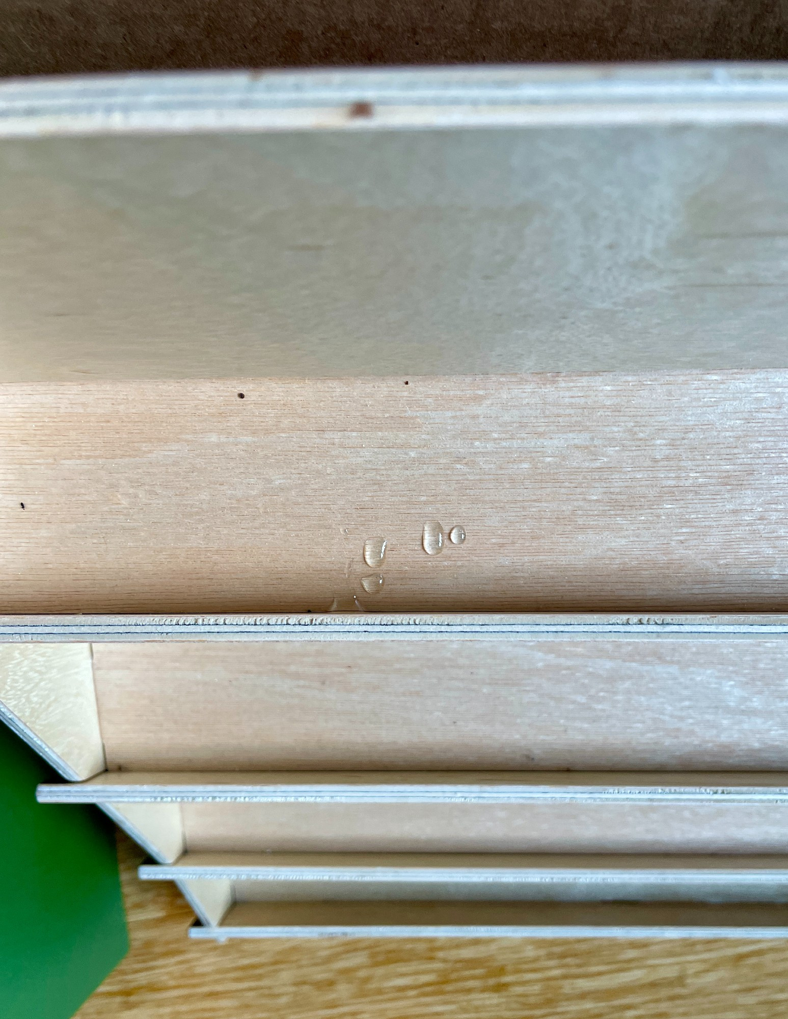 photo looking down at a birch wood card rack. A cluster of droplets that look like water are on the top shelf.