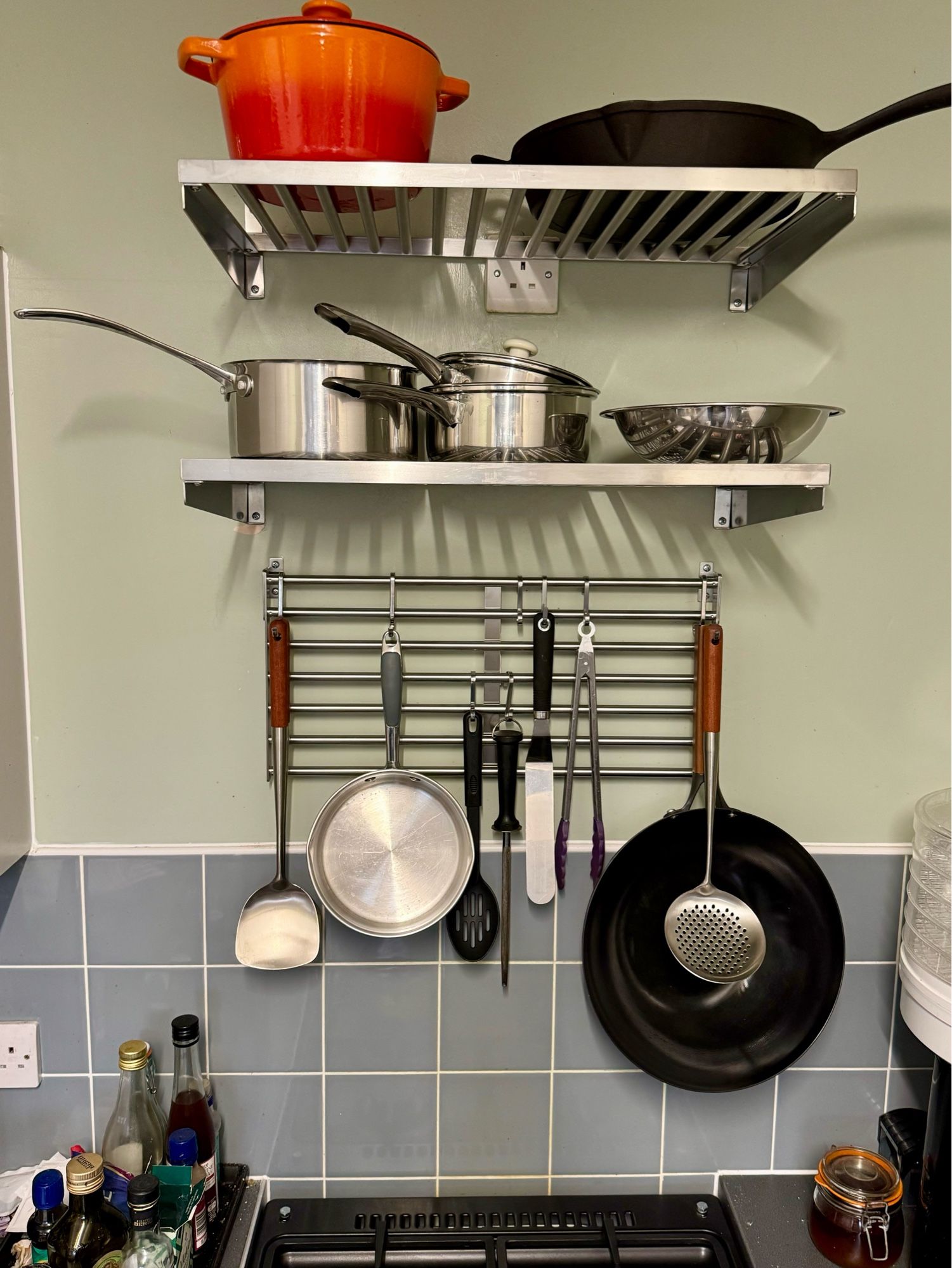 My favourite! A pan and utensil rack mounted on the wall above the backsplash of grey tiles. It has pots and pans and utensils hanging down off the hooks. Above that are two more industrial steel type shelves that now house all the pots and pans I had no space for!