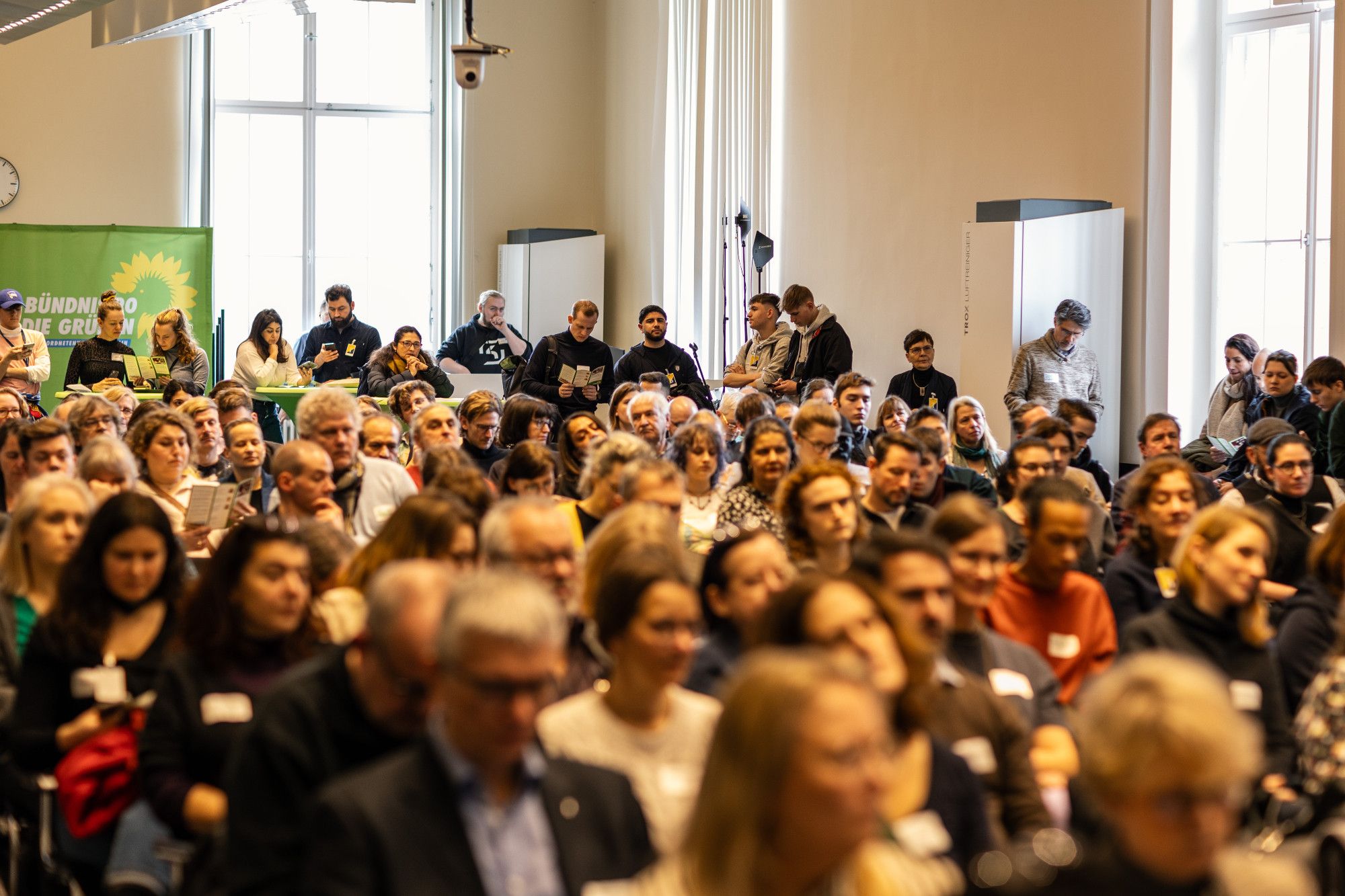 Ein Saal voller Menschen, die in Stuhlreihen sitzen. Die Gesichter sind unscharf.