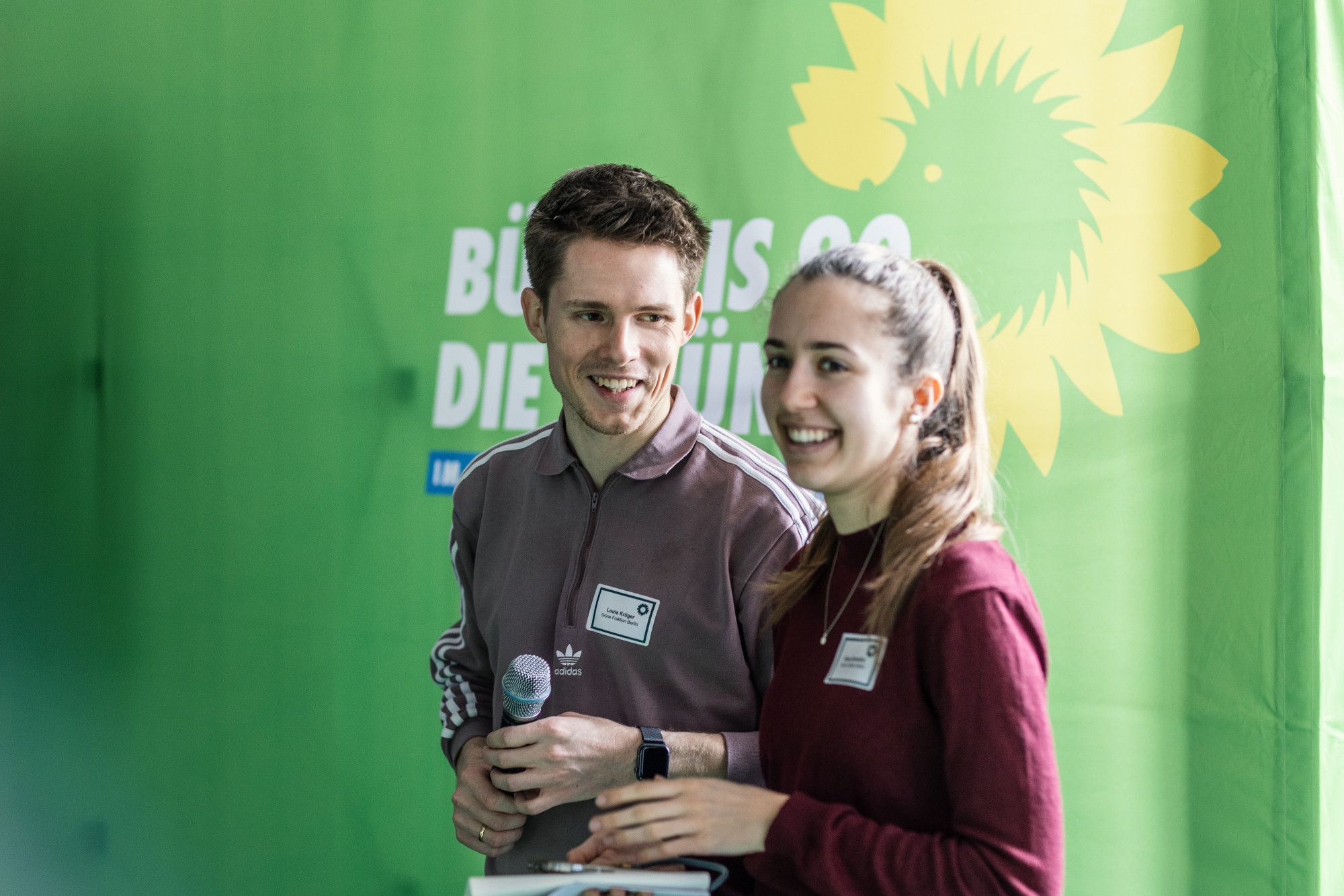 Louis Krüger und Klara Schedlich stehen nebeneinander vor einem grünen Banner und lächeln.