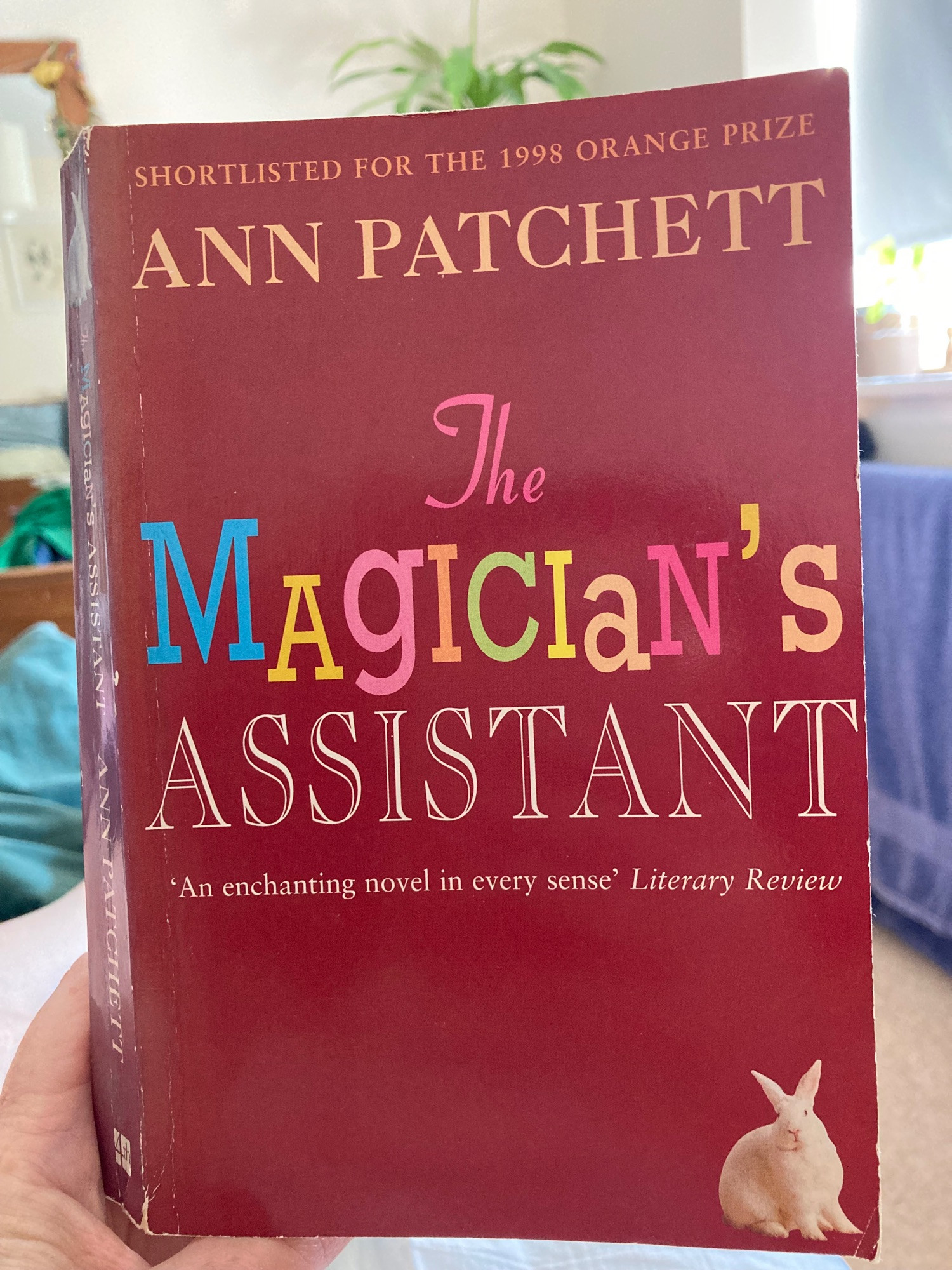 Dusky red paperback cover of Ann Patchett’s The Magician’s Assistant with multicoloured lettering and a white rabbit in the bottom rh corner.