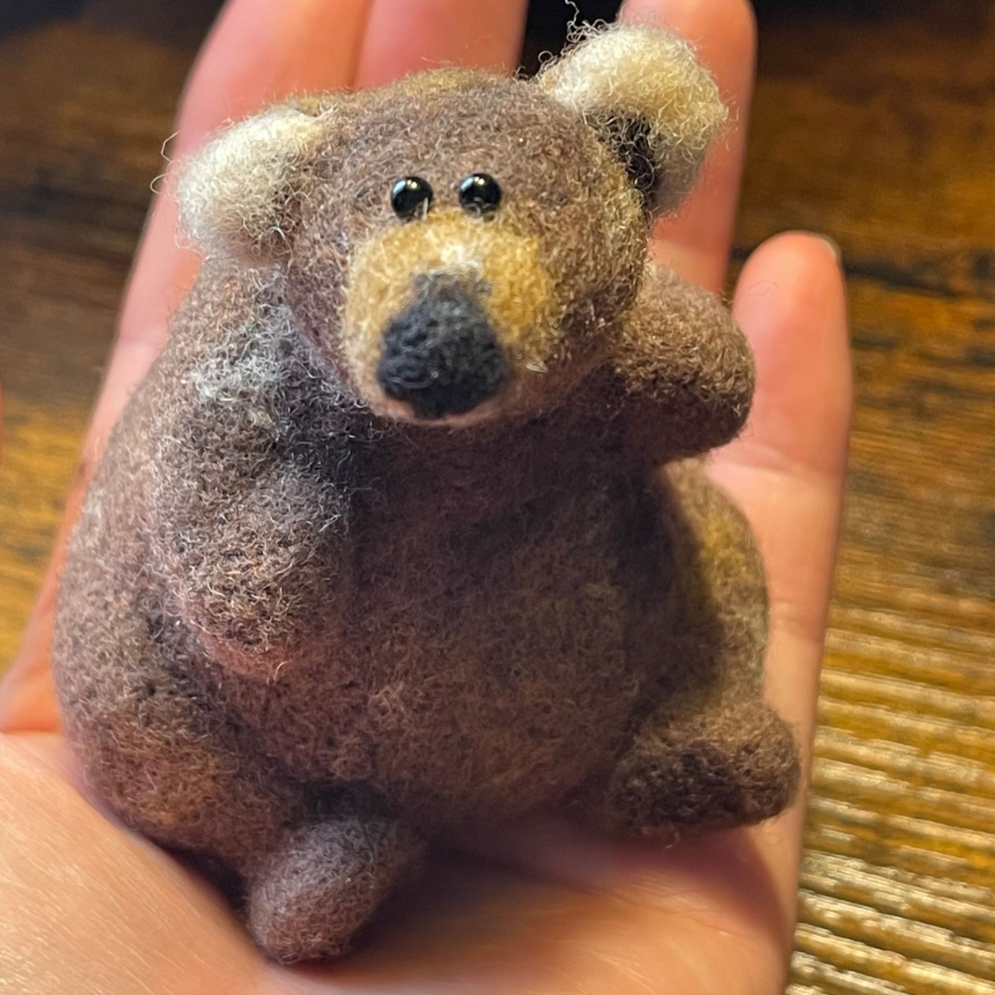 Needle felted bear sculpture of Bear #480 Otis. Bear is sitting in the palm of my hand and looking into the camera. His has one floppy right ear.