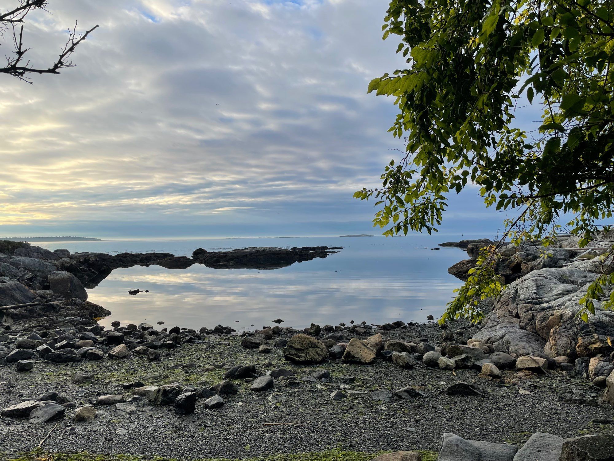 A small rocky cove: the water is perfectly still, and the rocks in the distance appear to be floating.