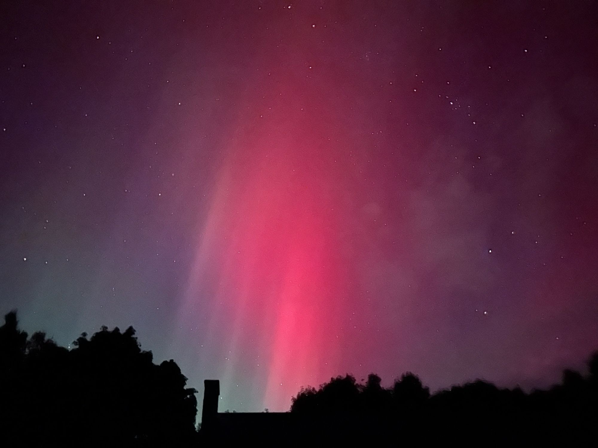 A red glow above the silhouette of a chimney and treetops