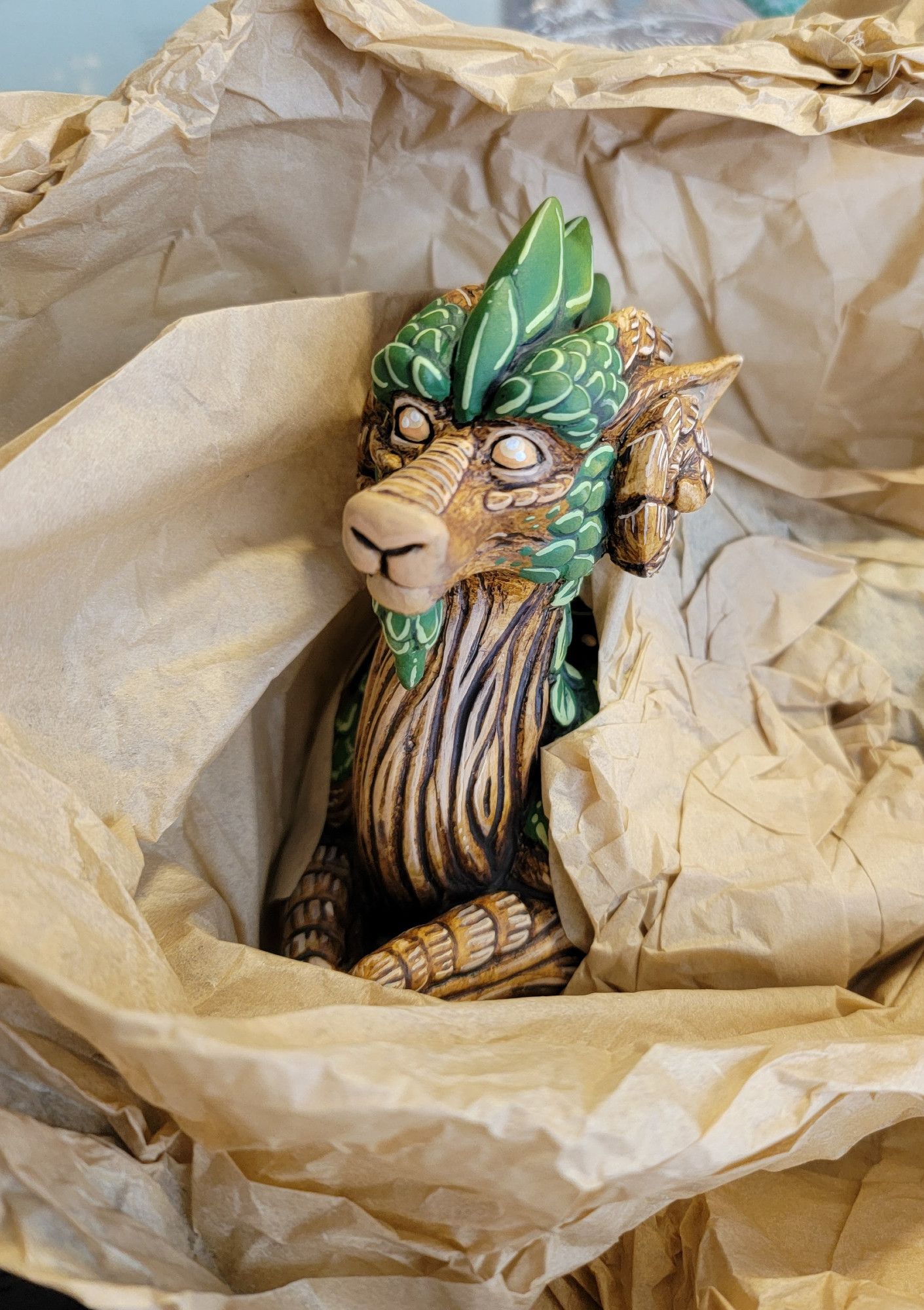 A mossy, leafy dragon sculpture peeking out from underneath some packing paper!