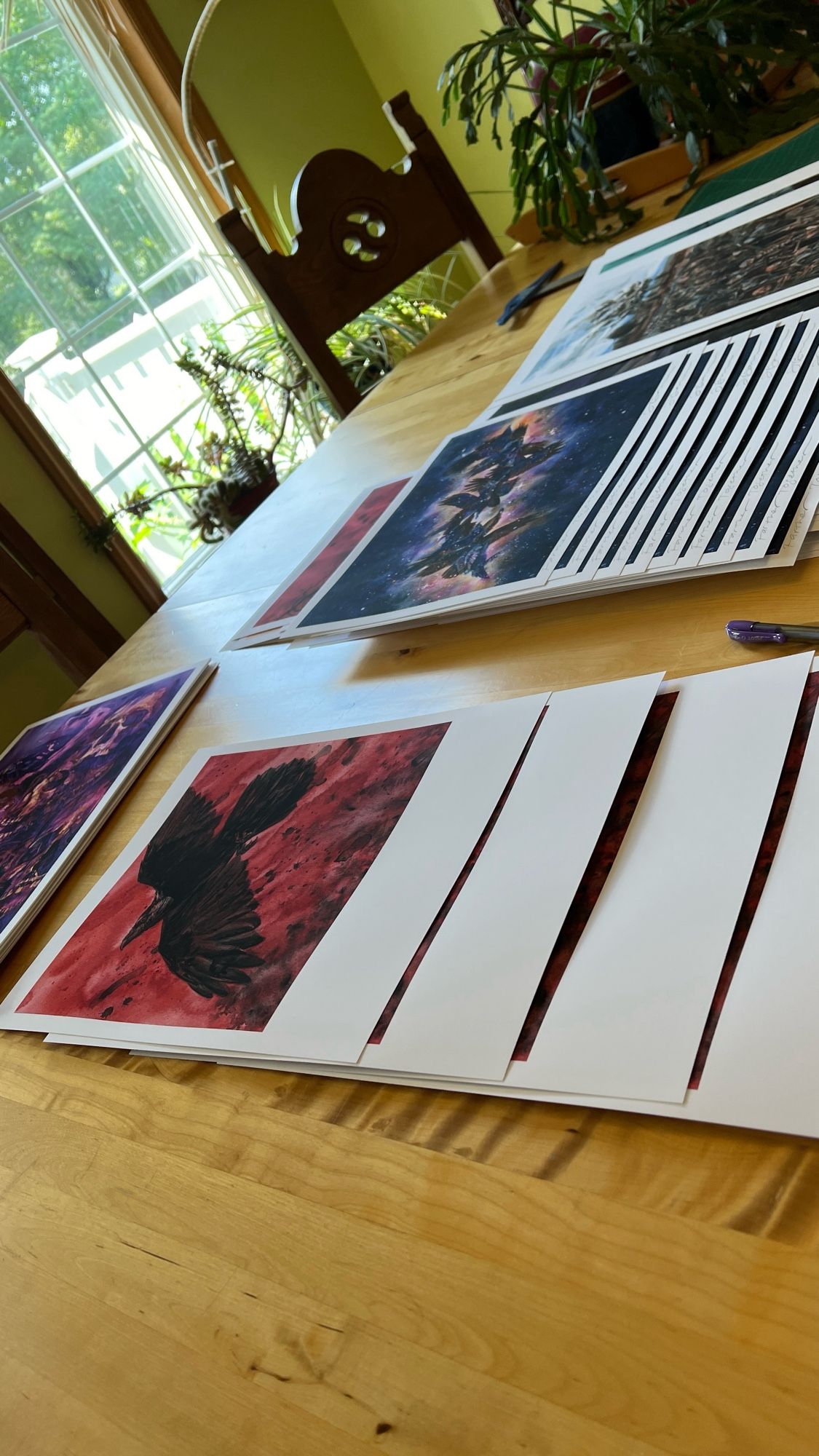 Many different art prints laid out on table for signing