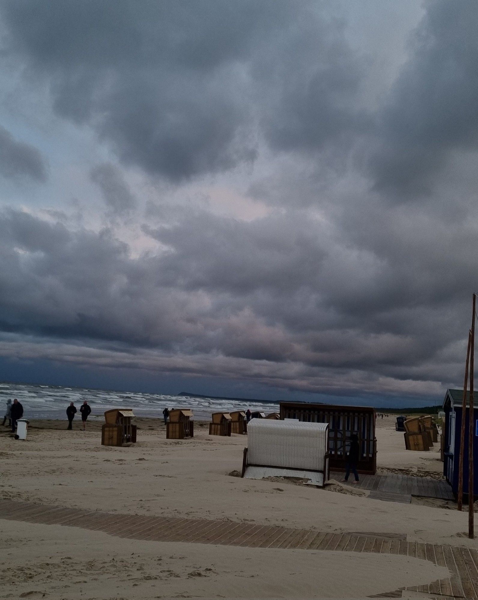 Am Strand von Usedom. Der Himmel ist bedeckt und fie Sonne geht unter 
Am Strand sind Strandkörbe