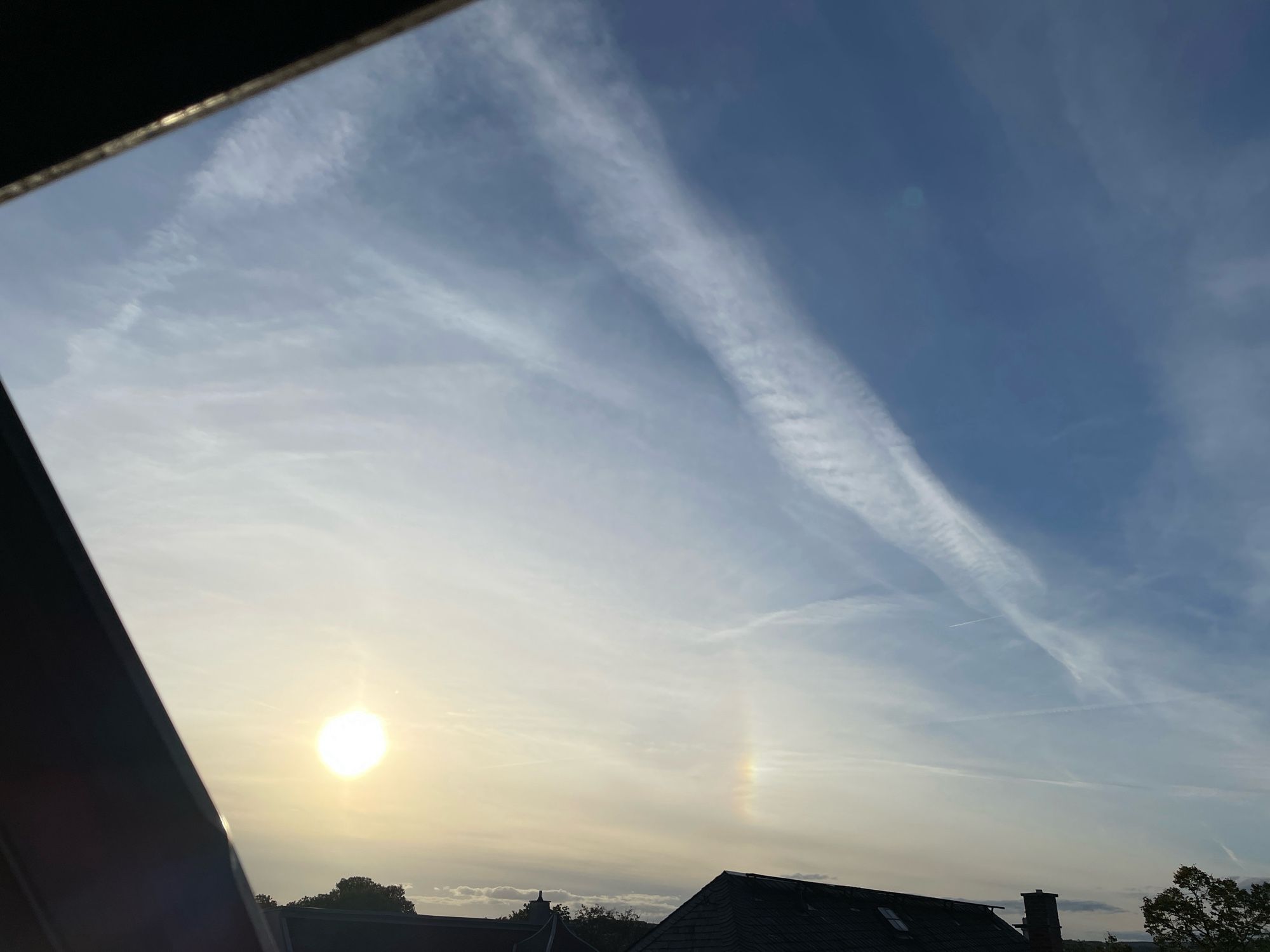 Sonne über dunklen Stadtdächern mit kleinem Ausschnitt aus dem Zirkumzenitalbogen: Er entsteht mittels Eiskristallen in sehr hohen Wolken.