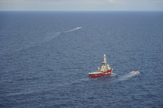 Aus der Luft aufgenommen. Die OPEN ARMS mitten auf dem Meer. Weiter hinten ist ein Boot mit unstetem Kurs zu erkennen. Ein RHIB macht sich gerade in voller Fahrt von der OA auf den Weg zu diesem Boot.