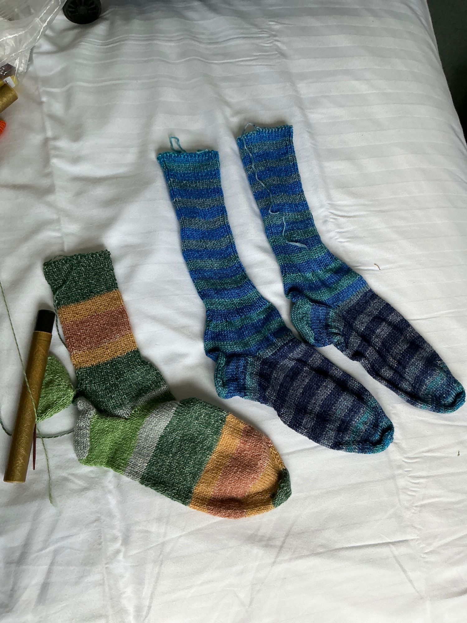 One green and orange striped handknitted sock, and two blue variegated striped handknitted socks.