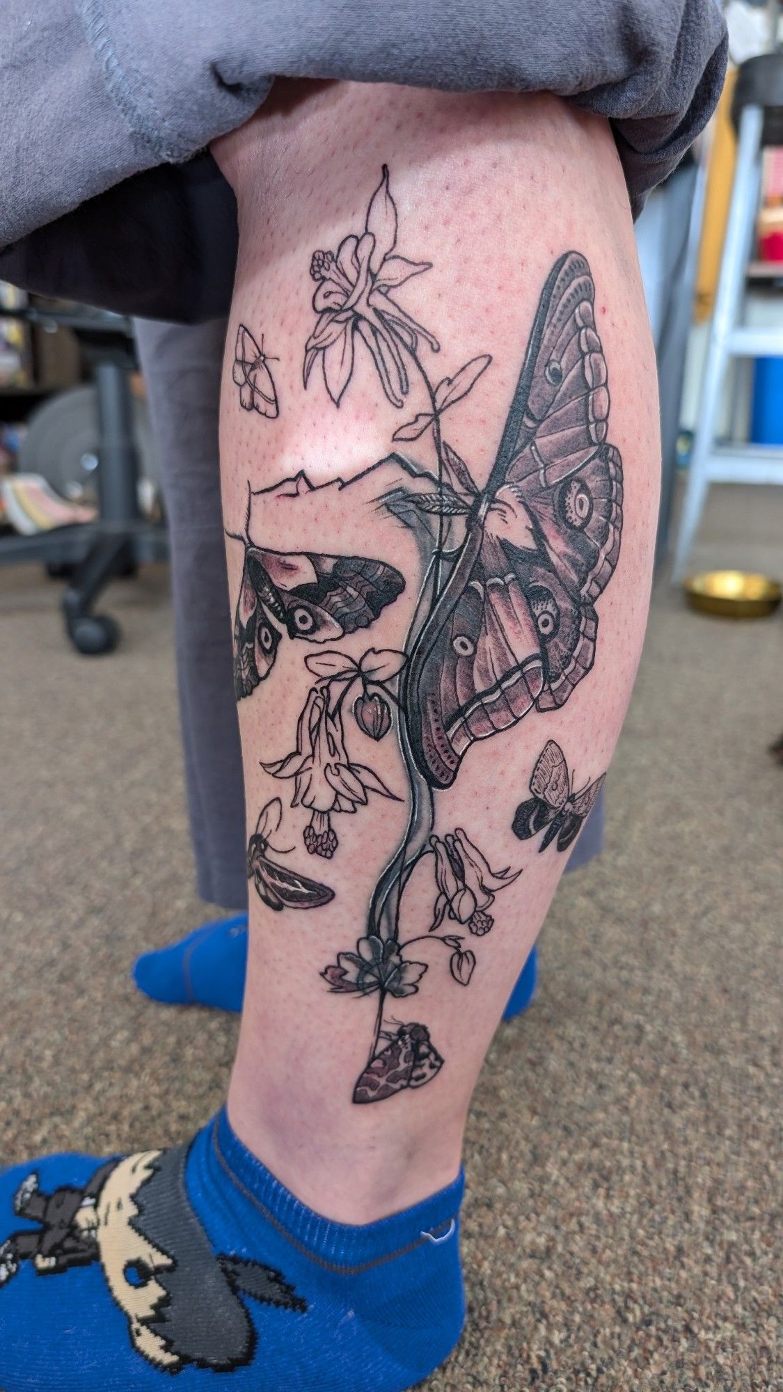 A calf tattoo featuring various different moths with columbine flowers