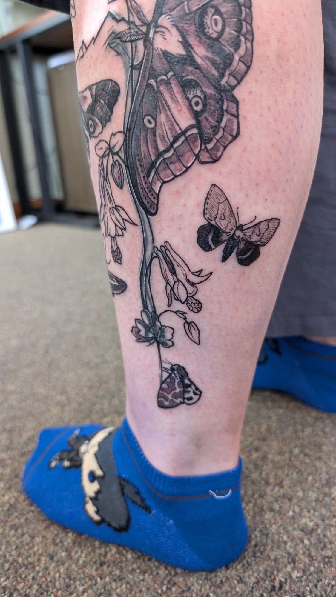 A calf tattoo featuring various different moths with columbine flowers