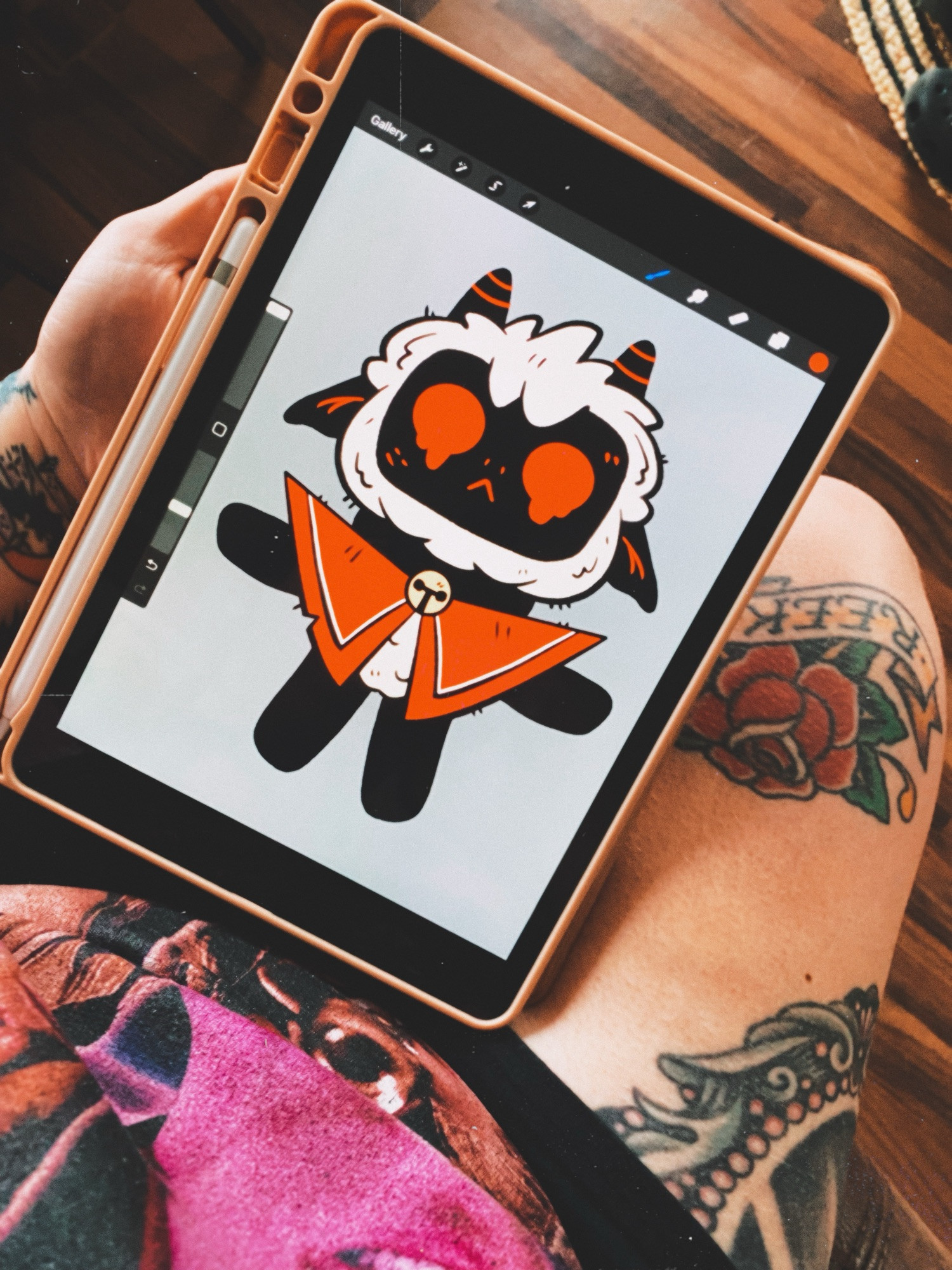 a photo of an ipad screen drawing. it’s a cartoon lamb from the video game cult of the lamb. his eyes are red and melty. the ipad is resting on meghan’s lap, her leg tattoos are visible