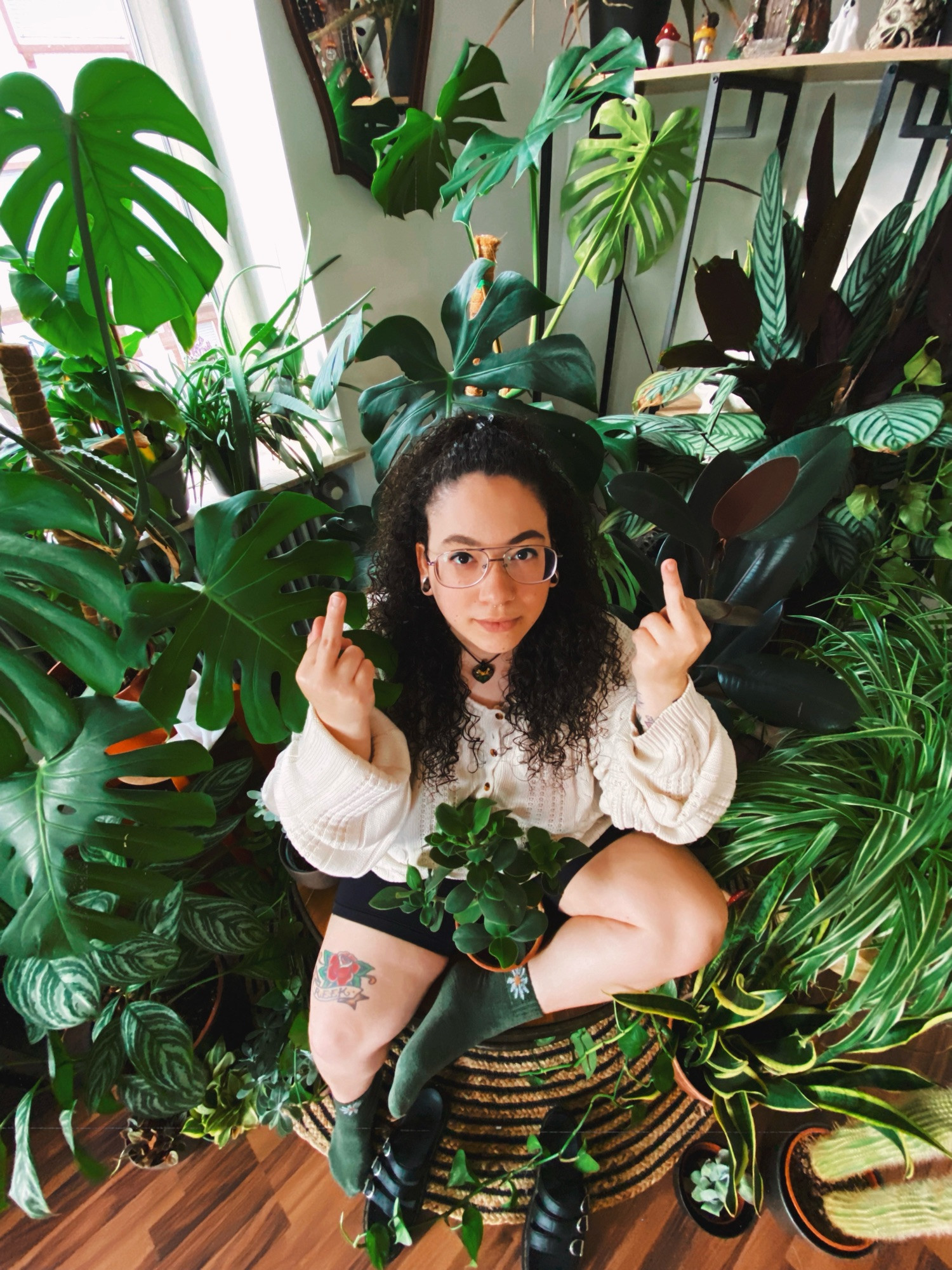 meghan sitting in the middle of 30+ house plants. the plants are all a vibrant green and have big beautiful leaves.