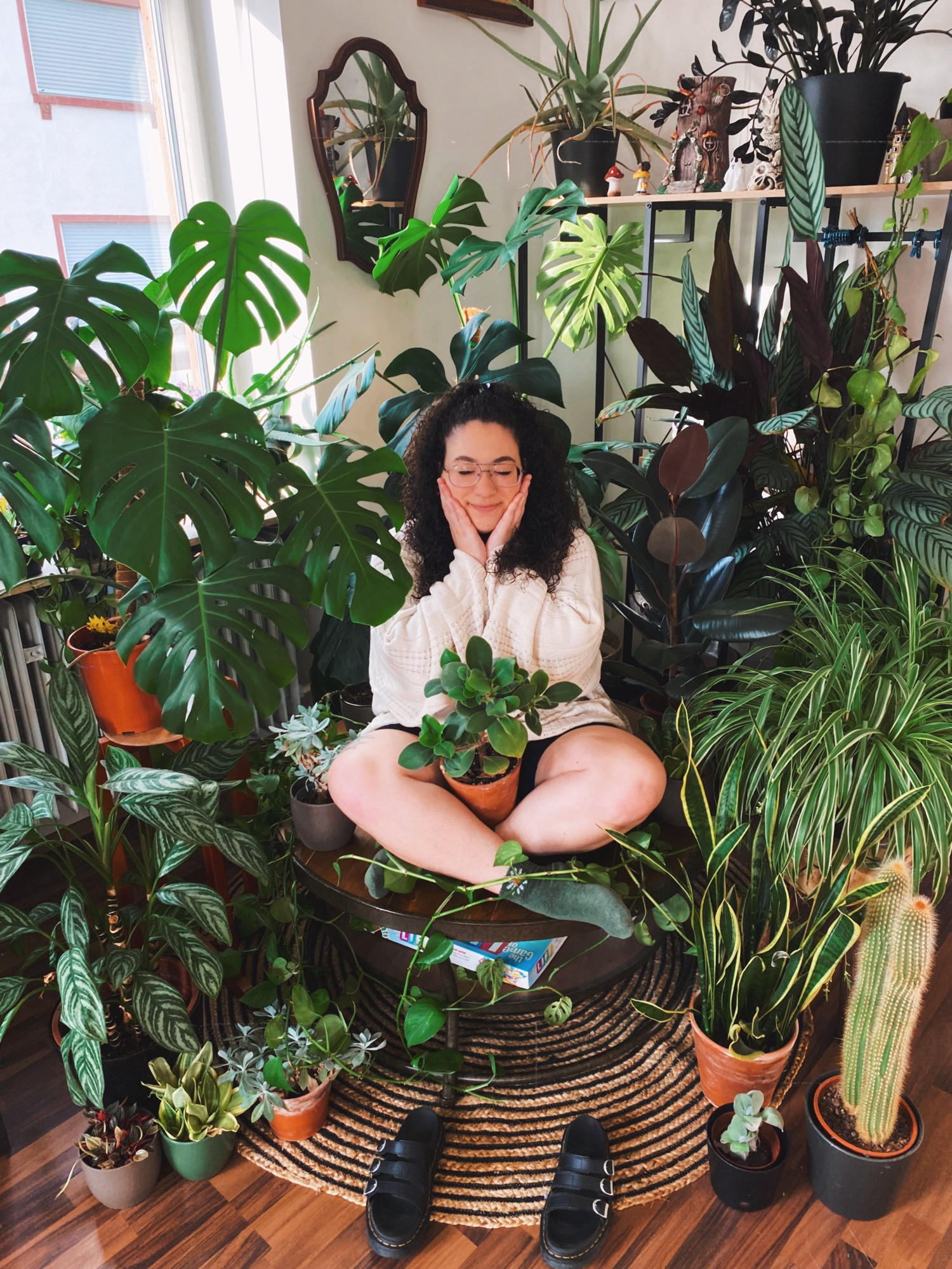 meghan sitting in the middle of 30+ house plants. the plants are all a vibrant green and have big beautiful leaves.