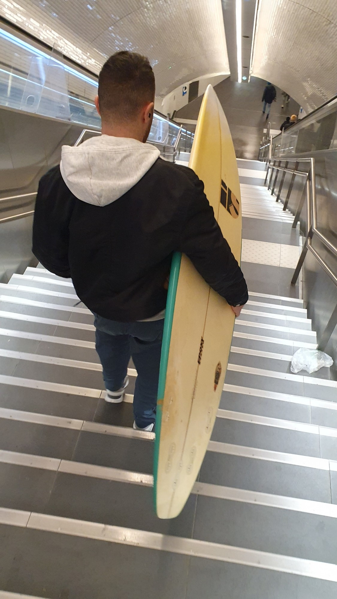 Un homme tient une planche de surf dans les couloirs du métro