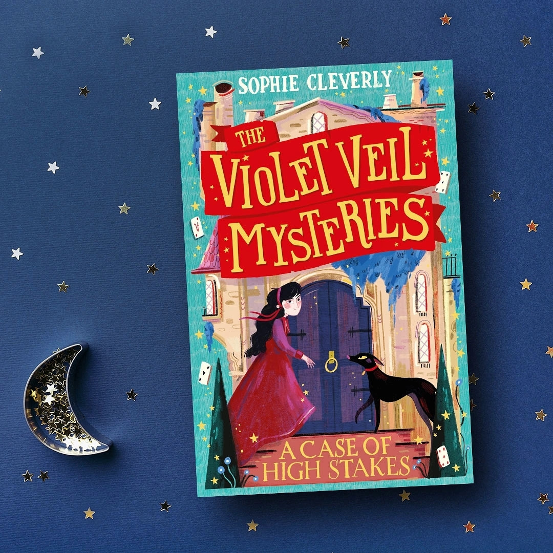 A copy of my new book The Violet Veil Mysteries - A Case of High Stakes. The cover shows Violet and her dog Bones at the door of a mysterious manor. The background is blue and covered with stars and a moon.