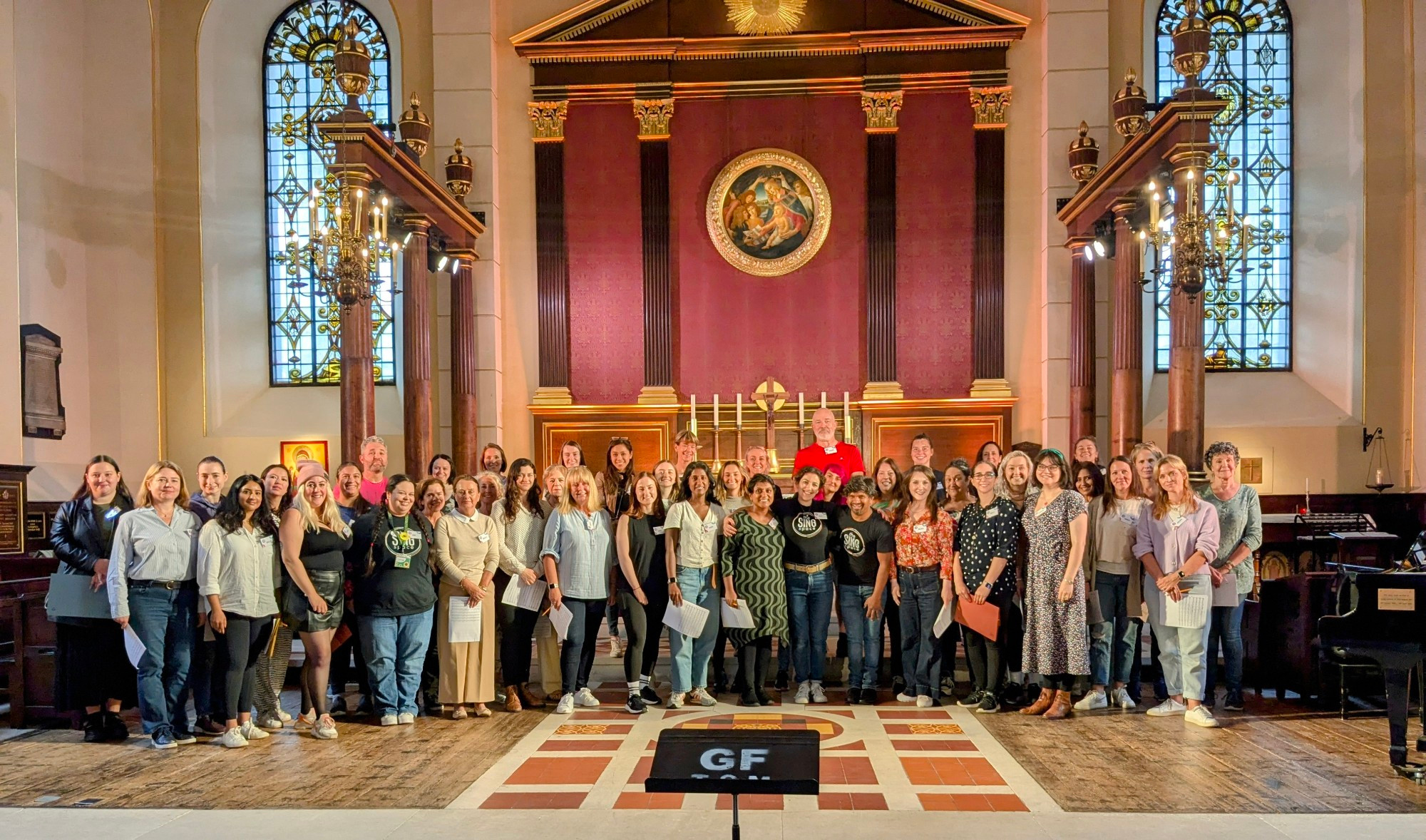 Sing Space choir group posed for photo inside the Actors' Church (St. Paul's) Covent Garden, with stained glass windows in the background.