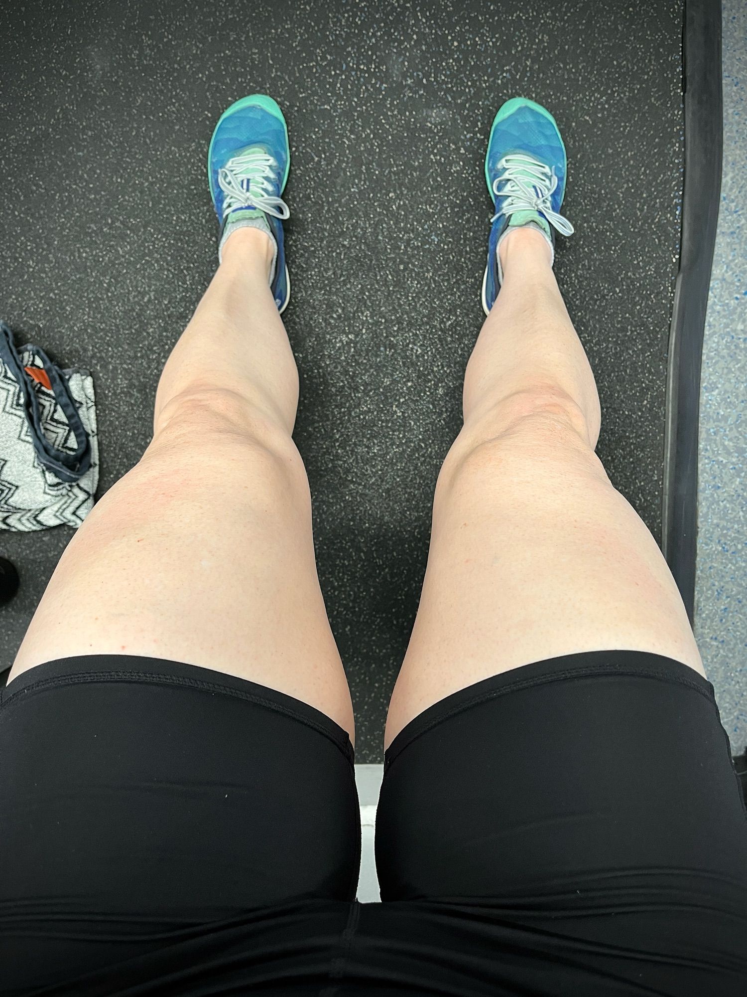 Photo looking down at my legs in the gym as I lean against the wall. It’s quad day so I have a pump on in my little black bike shorts. The melons look set to crush…