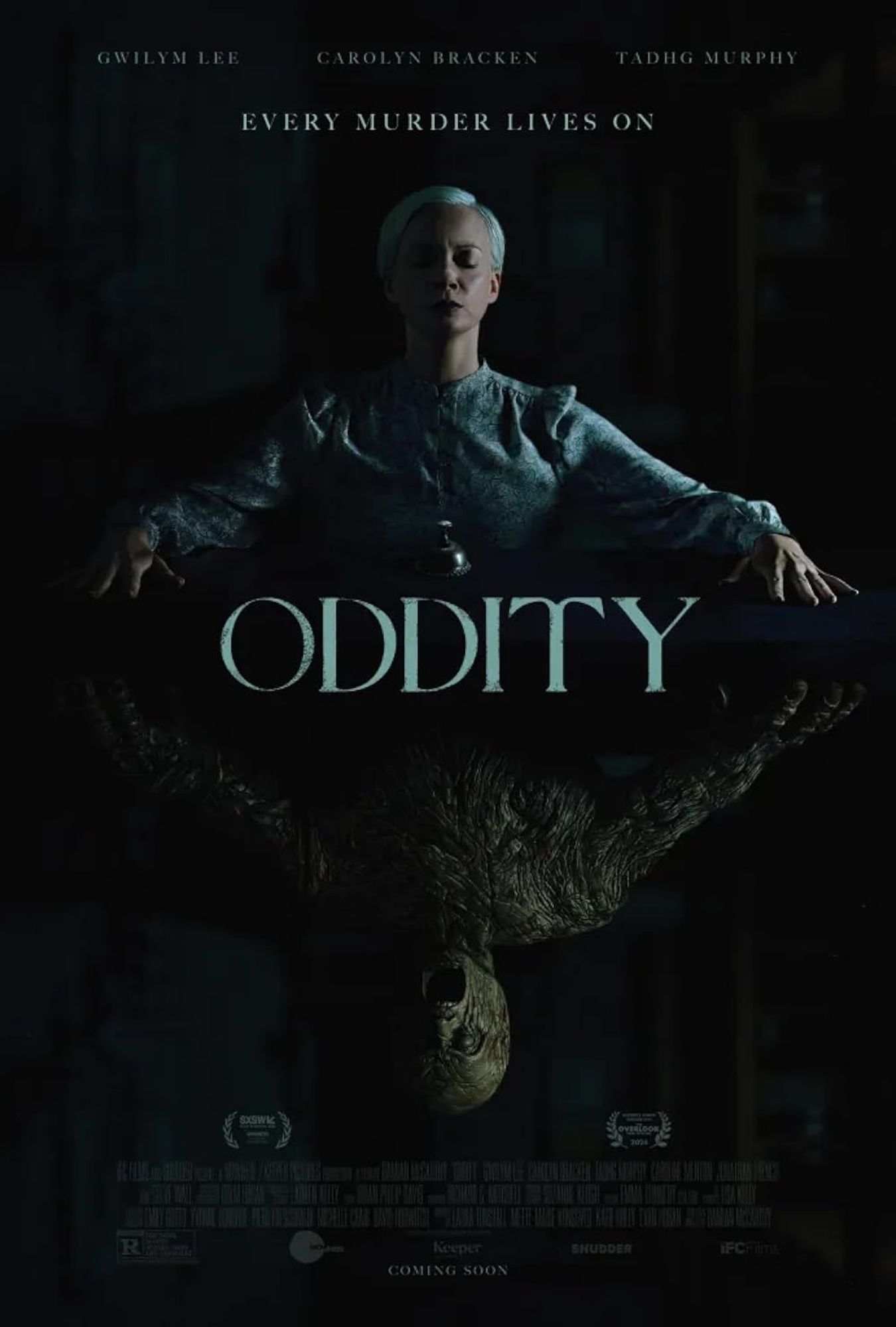 Movie poster for the horror film Oddity. A woman with short blond hair is featured at the top sitting at a table with her hands on the table top she seems to be in meditation. Mirrored below her is a wooden golem creature in a similar pose. It's mouth is open.