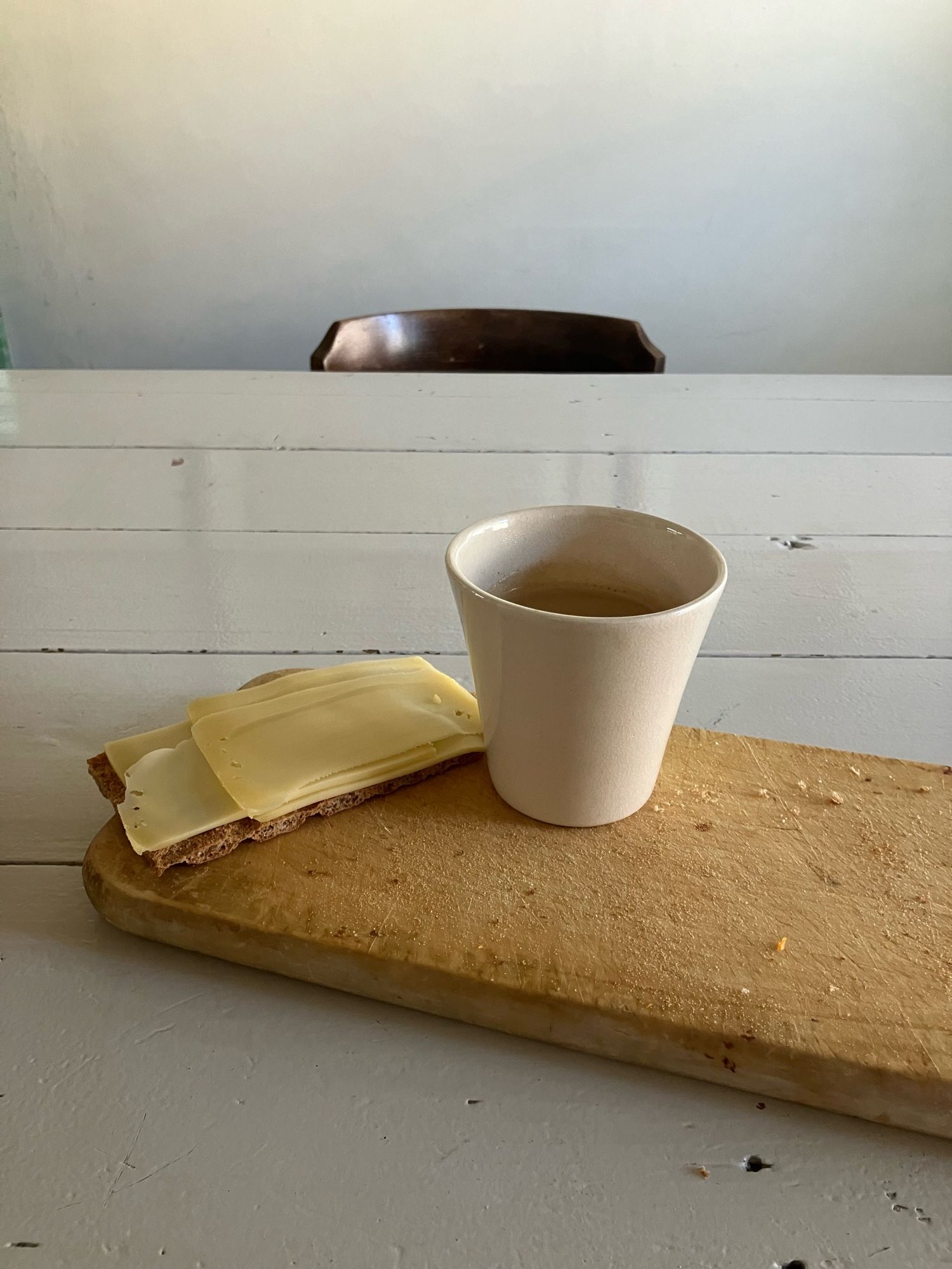 Wit Houten Tafelblad en houten broodplankje, daarop bakkie koffie en krekker met kaas