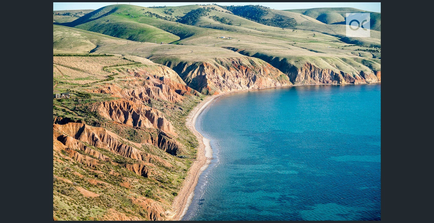 aerial shot of a beach with large cliffs, and hills in the background. The hills form the hanging-wall of an active reverse fault