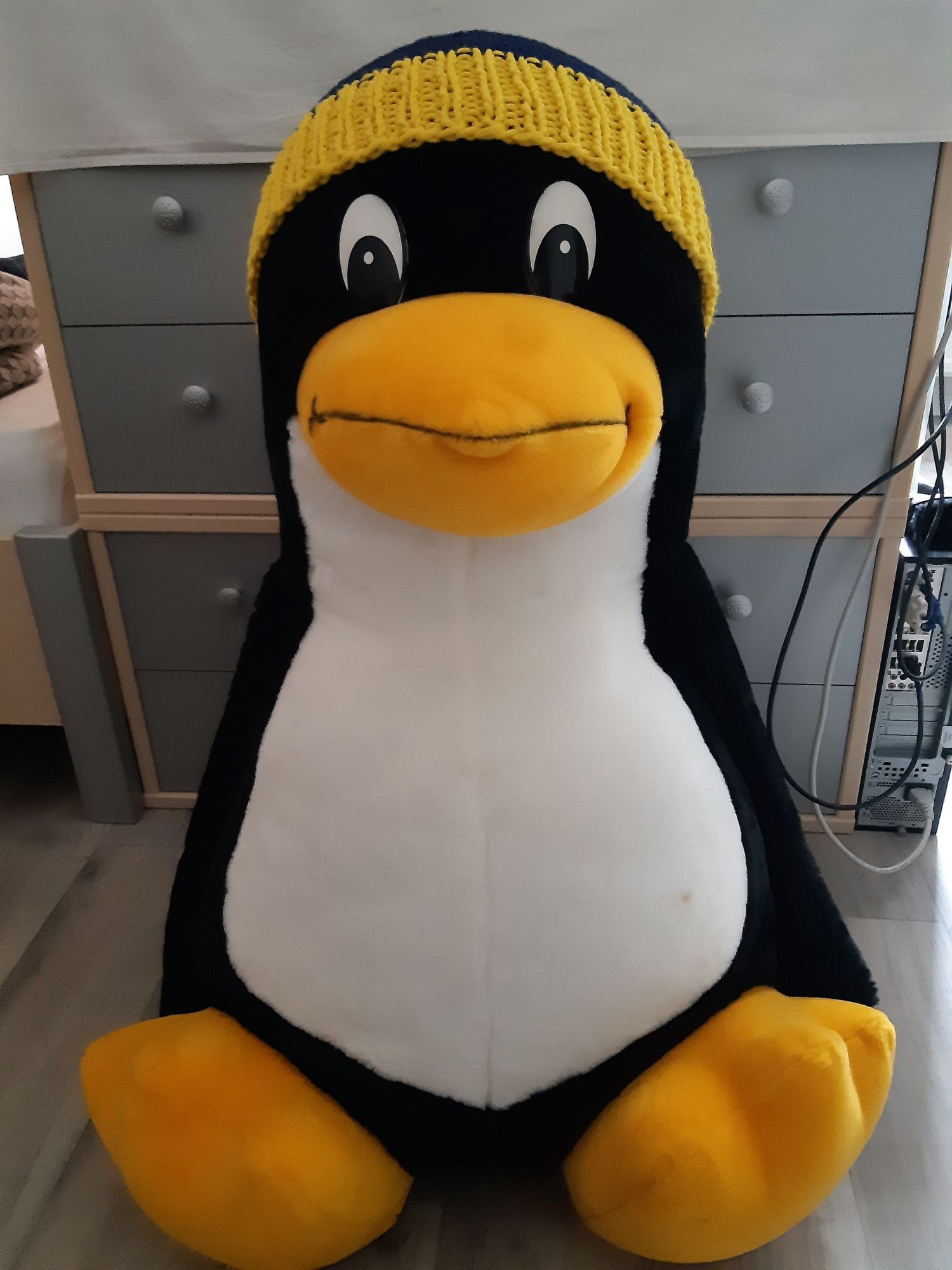 Ein großer Plüsch-Tux sitzt auf dem Boden und schaut dich an.