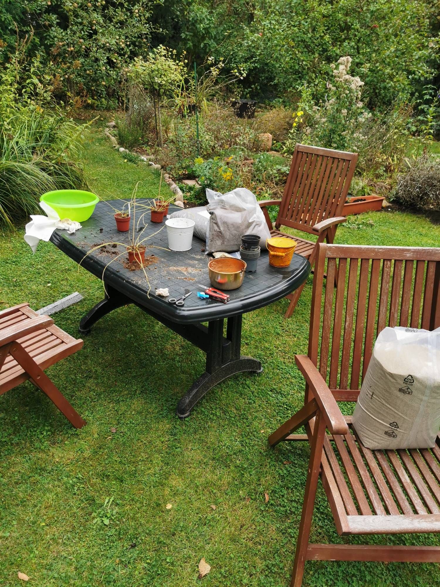 Ein vollbepackter Gartentisch mit Säcken verschiedener Substrate und Blumentöpfe.