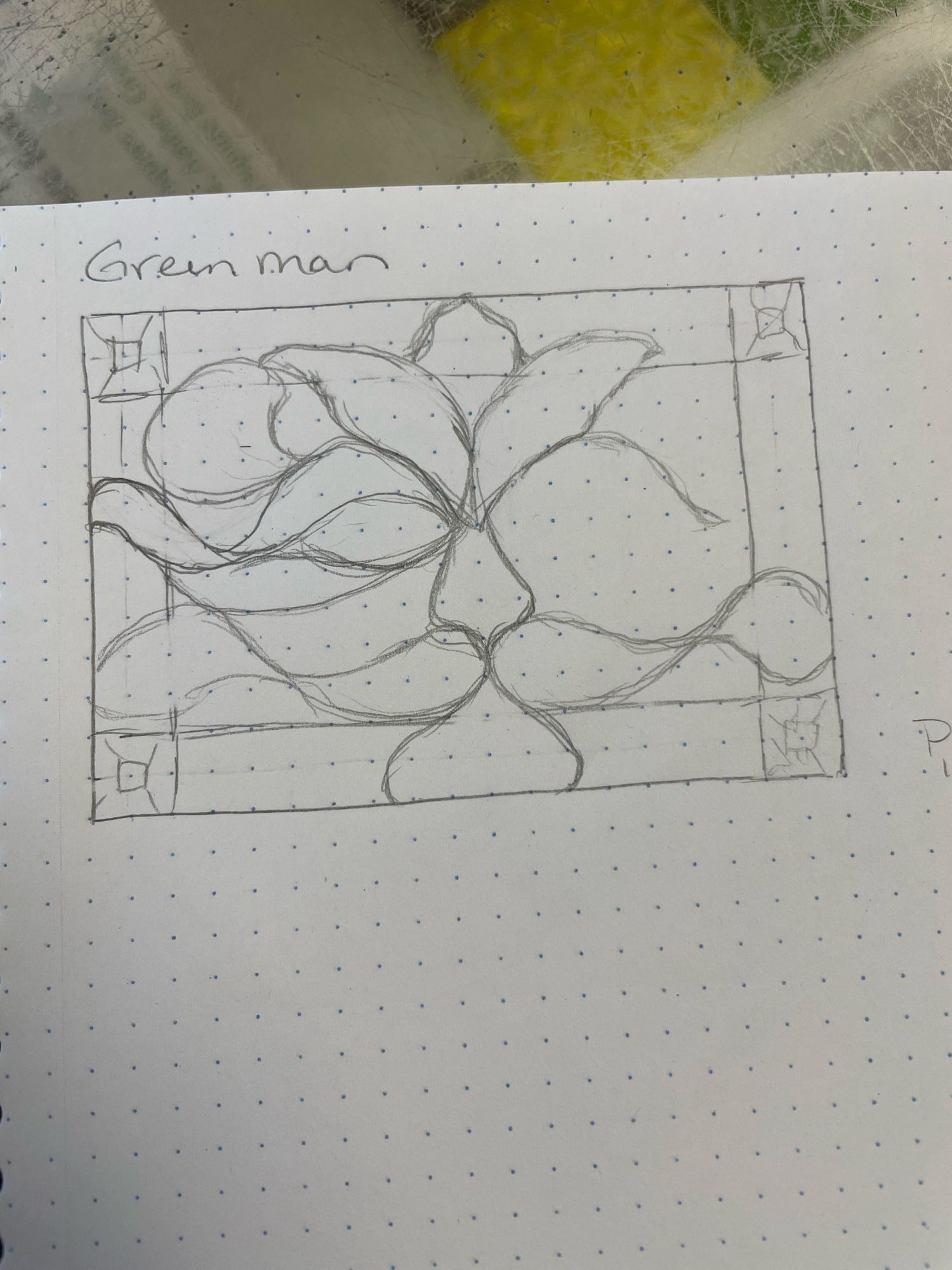 A page of dot grid paper with a rough, unfinished pencil sketch of a traditional green man face inside of a rectangular border