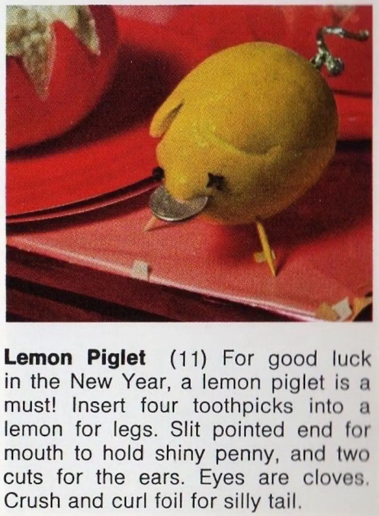 A photo of a lemon piglet with a description of it that reads: Lemon Piglet (11) For good luck in the New Year, a lemon piglet is a must! Insert four toothpicks into a lemon for legs. Slit pointed end for mouth to hold shiny penny, and two cuts for the ears. Eyes are cloves. Crush and curl foil for silly tail.