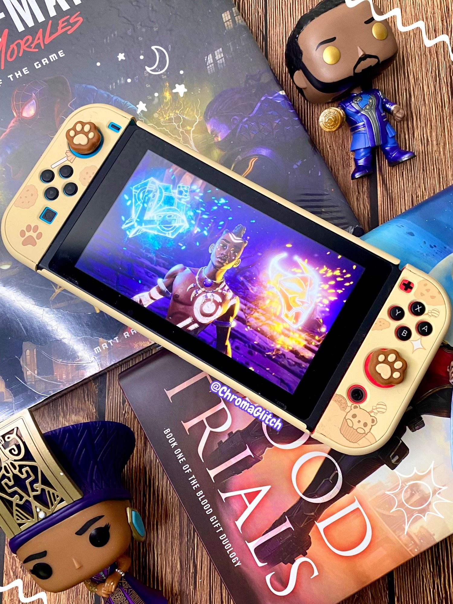 Image of a flat lay with a Nintendo Switch in the center, surrounded by books and funko pops. On the screen is  a screenshot of art for The Tale of Kenzera: Zau.