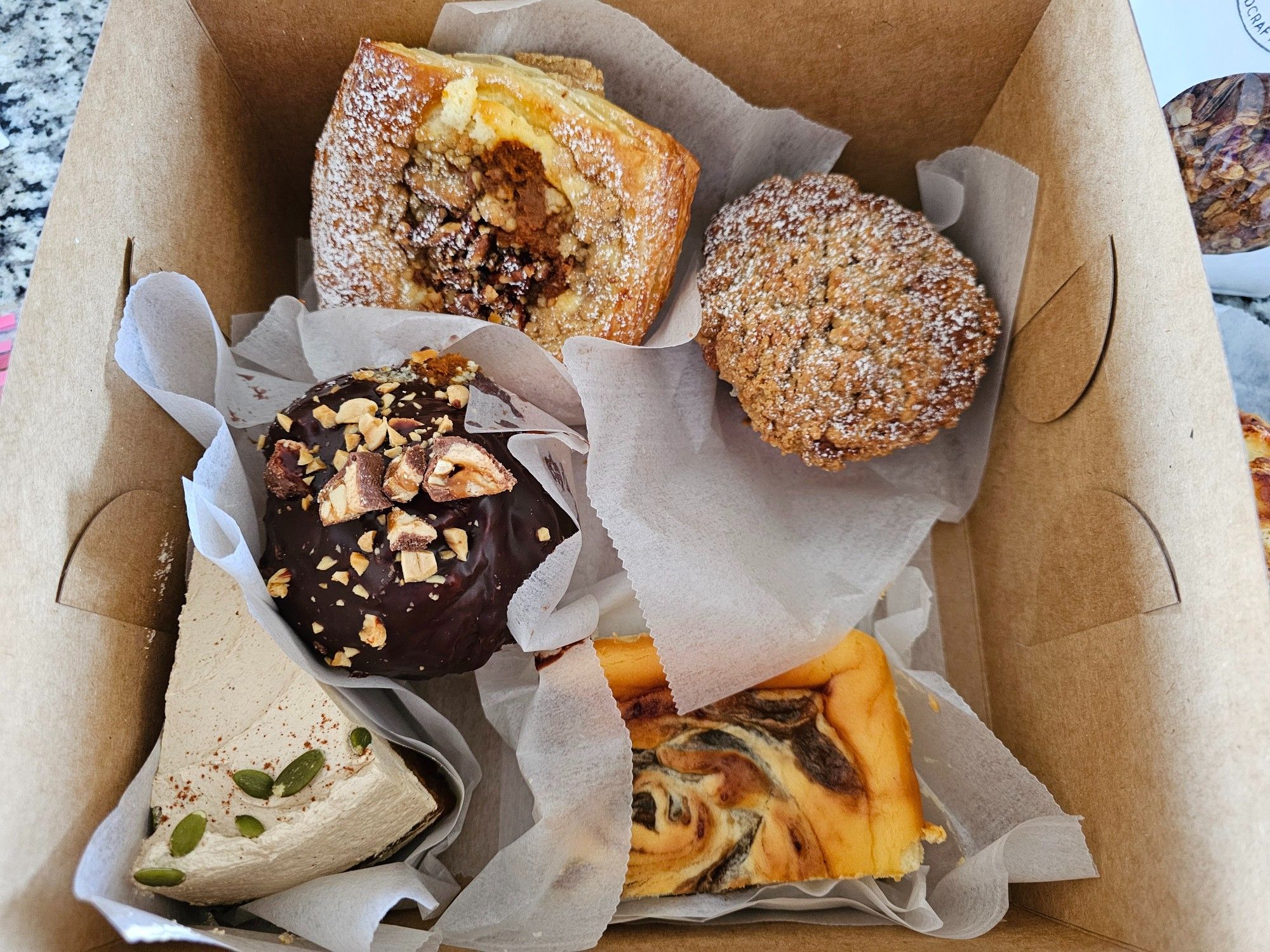 A collection of baked goods including: a pumpkin candied pecan scone, an apple crumb muffin, a snickers cruffin, a punpkin brown sugar spice cake slice, and an apple butter cheesecake