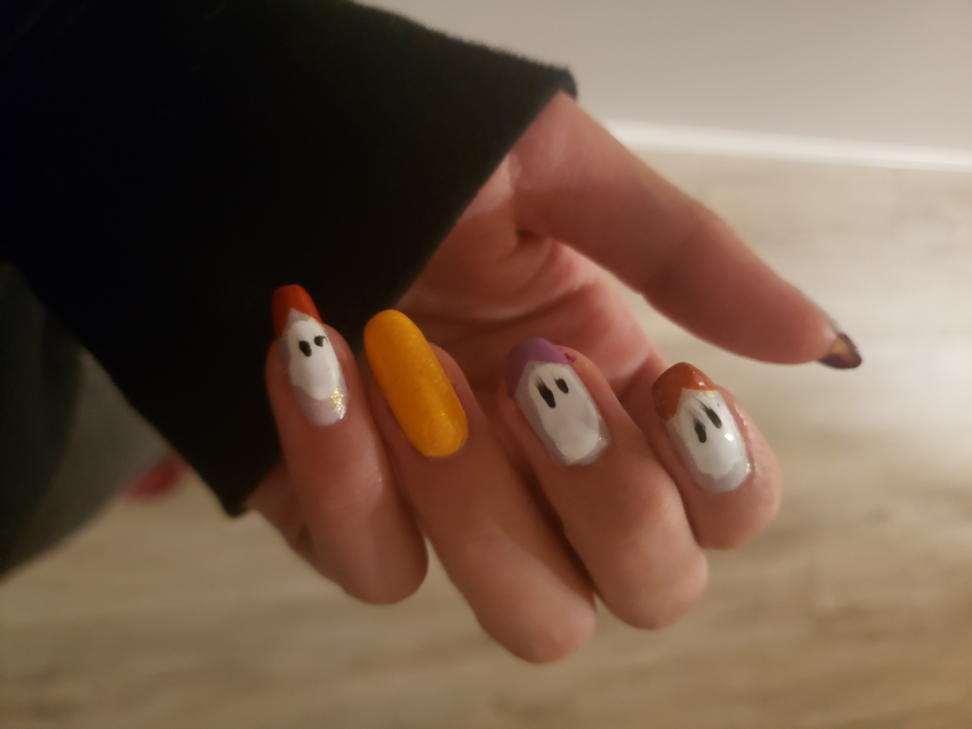 Nails painted of little ghosts with alternating colour French tips in dark orange and mauve, with a butterscotch yellow accent nail