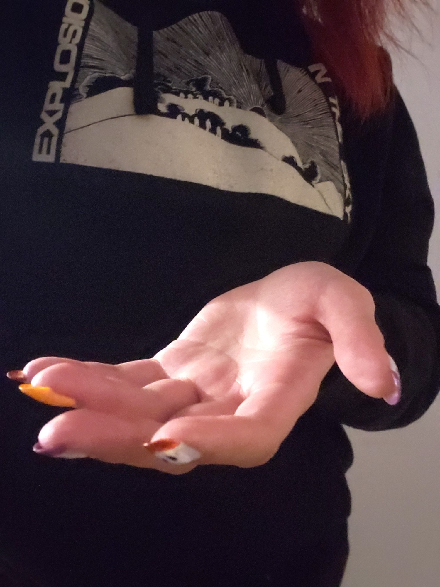 A hand with painted nails extended to camera in front of a black hoodie