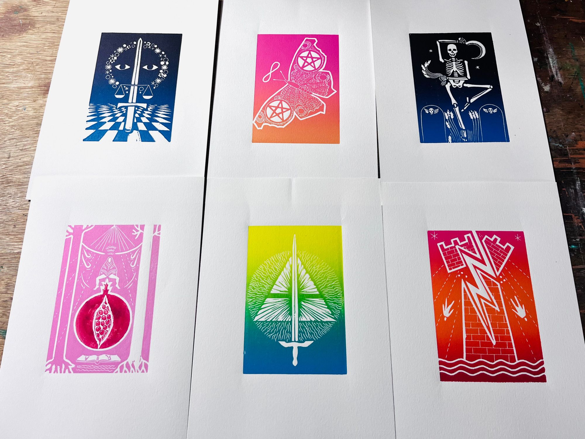 a photo of 6 brightly-coloured lino prints of tarot cards - Justice, 2 of pentacles, Death, High Priestess, Ace Swords and the Tower