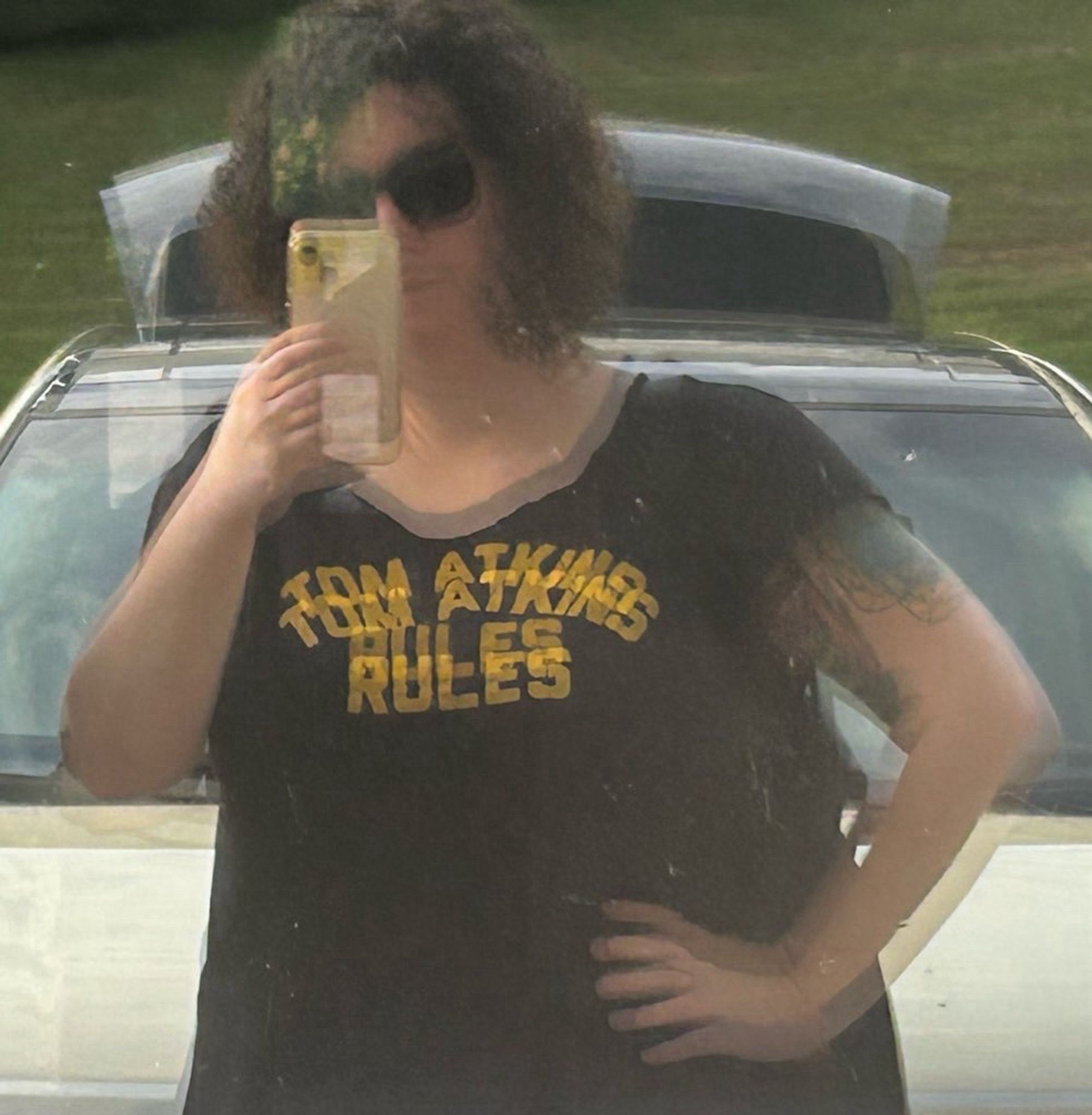 A blurry window reflection picture of Jessica wearing a t-shirt that says, “Tom Atkins rules”