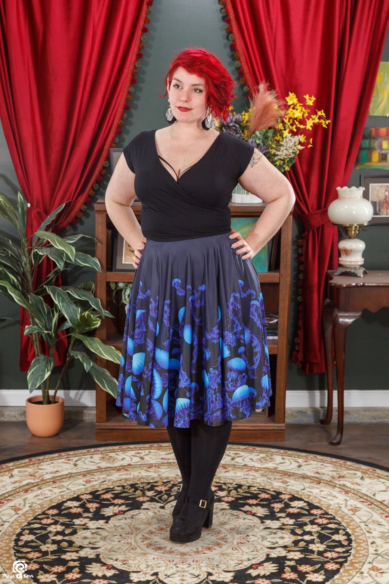 image of a mid size model wearing a black faux wrap crop top and a midi skirt. the skirt is a navy almost-black color with paintings of vibrant blue jellyfish across it.