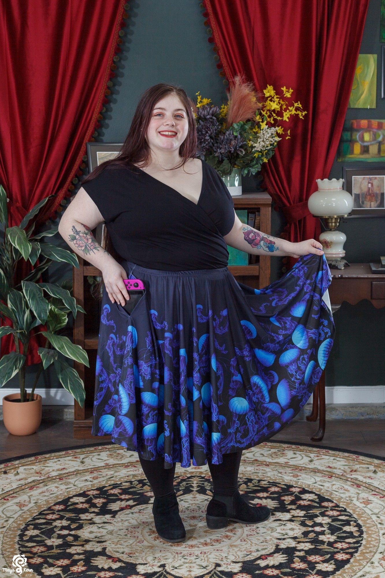 image of a plus size model wearing a black faux wrap crop top and a midi skirt. the skirt is a navy almost-black color with paintings of vibrant blue jellyfish across it.