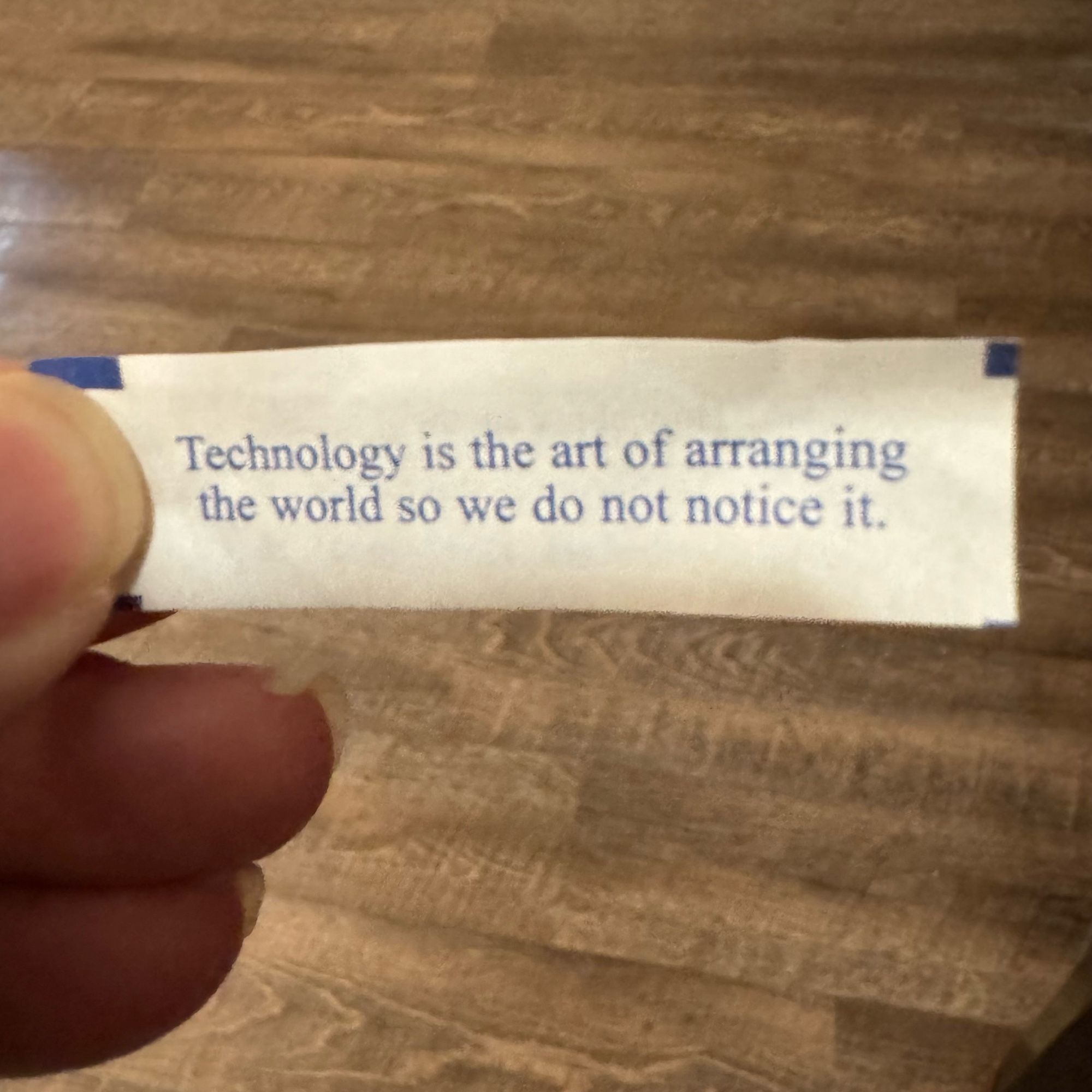 A fortune cookie fortune that reads “Technology is the art of arranging the world so we do not notice it.”