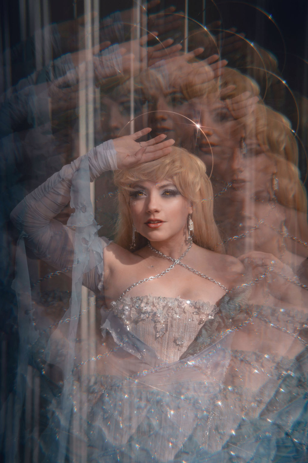 portrait photo of a woman with blonde hair and a gold halo wearing a sparkly gown with chains. a prism effect reflects copies of her around the center of the image.