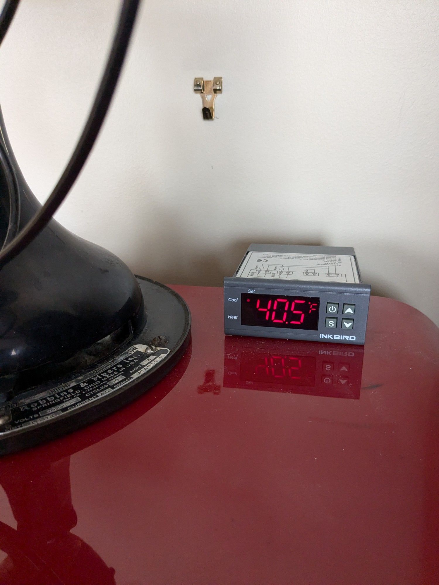 A digital temperature controller reading 40.5° f. It's on top of a red fridge, and the controls of an antique fan are visible to the left.