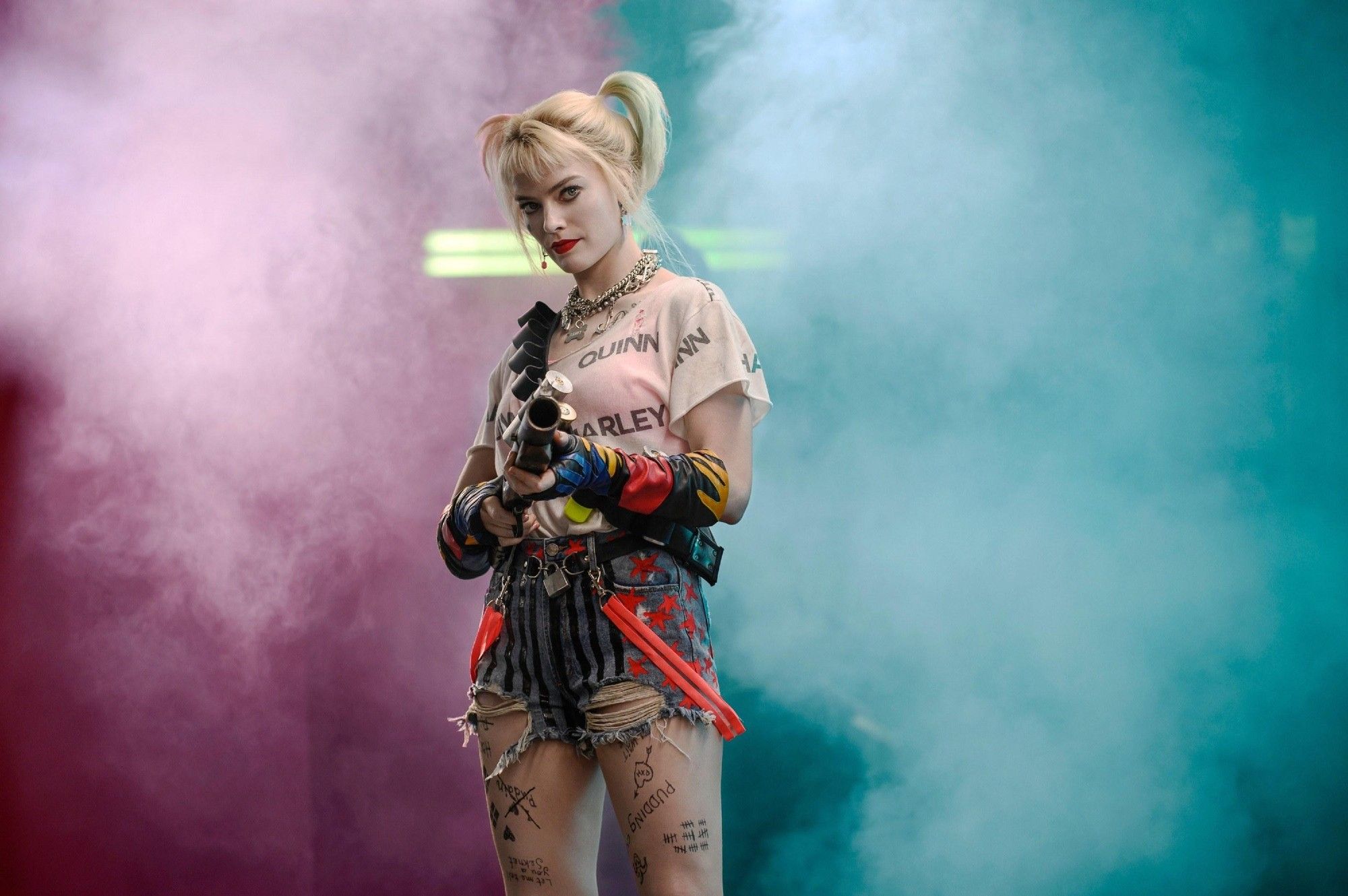 Harleen Quinzel played by Margot Robbie wielding a gas grenade gun. She's flanked by pink and light blue clouds of gas.