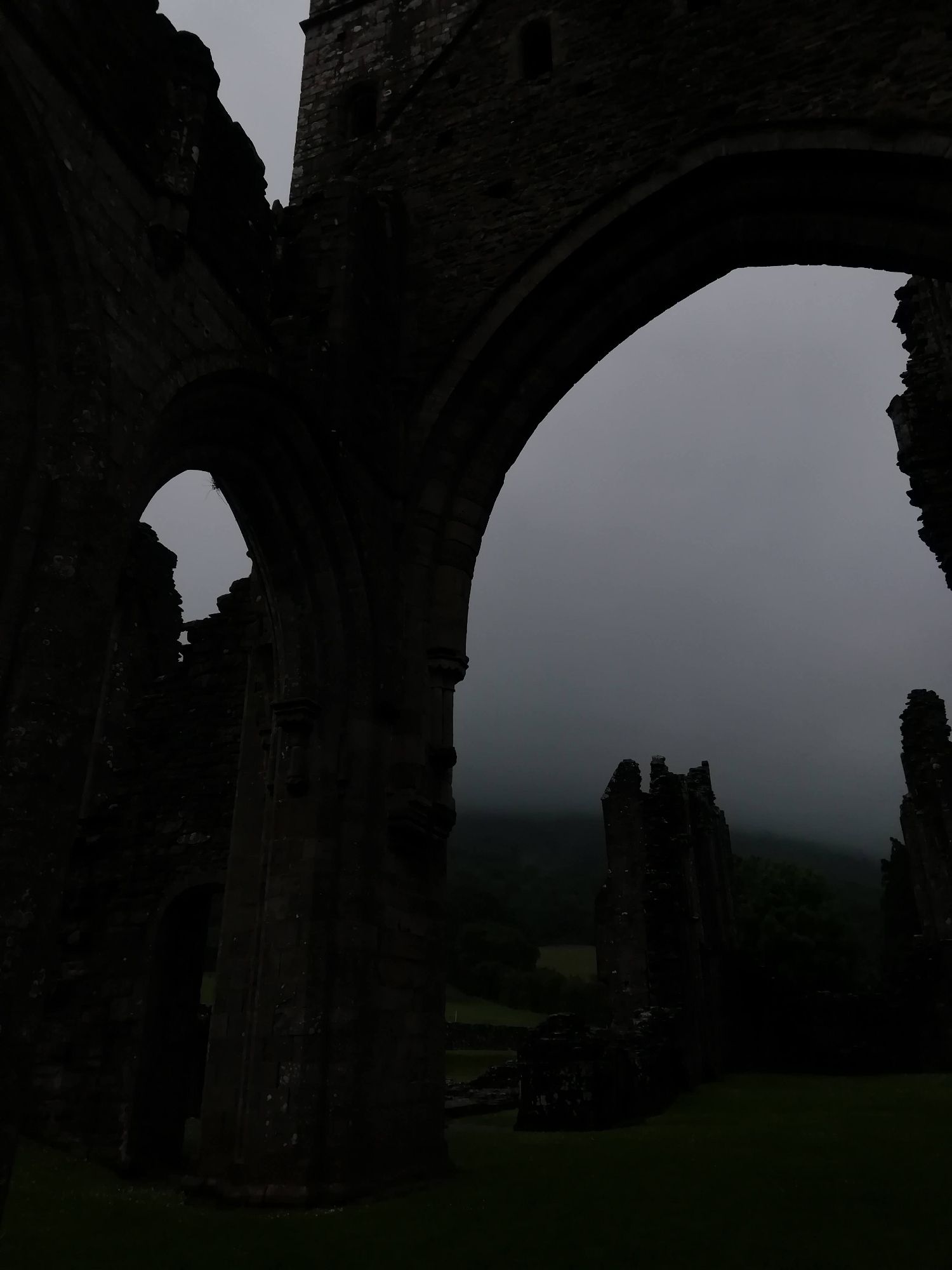 It picture of the big stone arch.. It was part of building once, but people killed it long ago and so now it mostly dead inside. It just bits left like ribs and bones and it do quiet things alone.
The bones is black like they been built of darkness and in the archway, stones look out and seem bit shocked, big cloud have swallowed most the world. 
Troop stand inside the building ghost and wonder what the stones seen 🌿