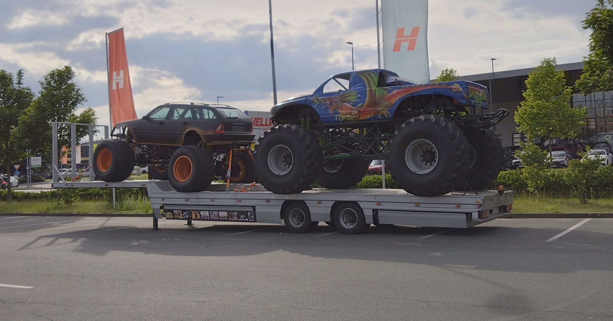 Zwei Monstertrucks auf einem LKW Tieflader auf einem Parkplatz