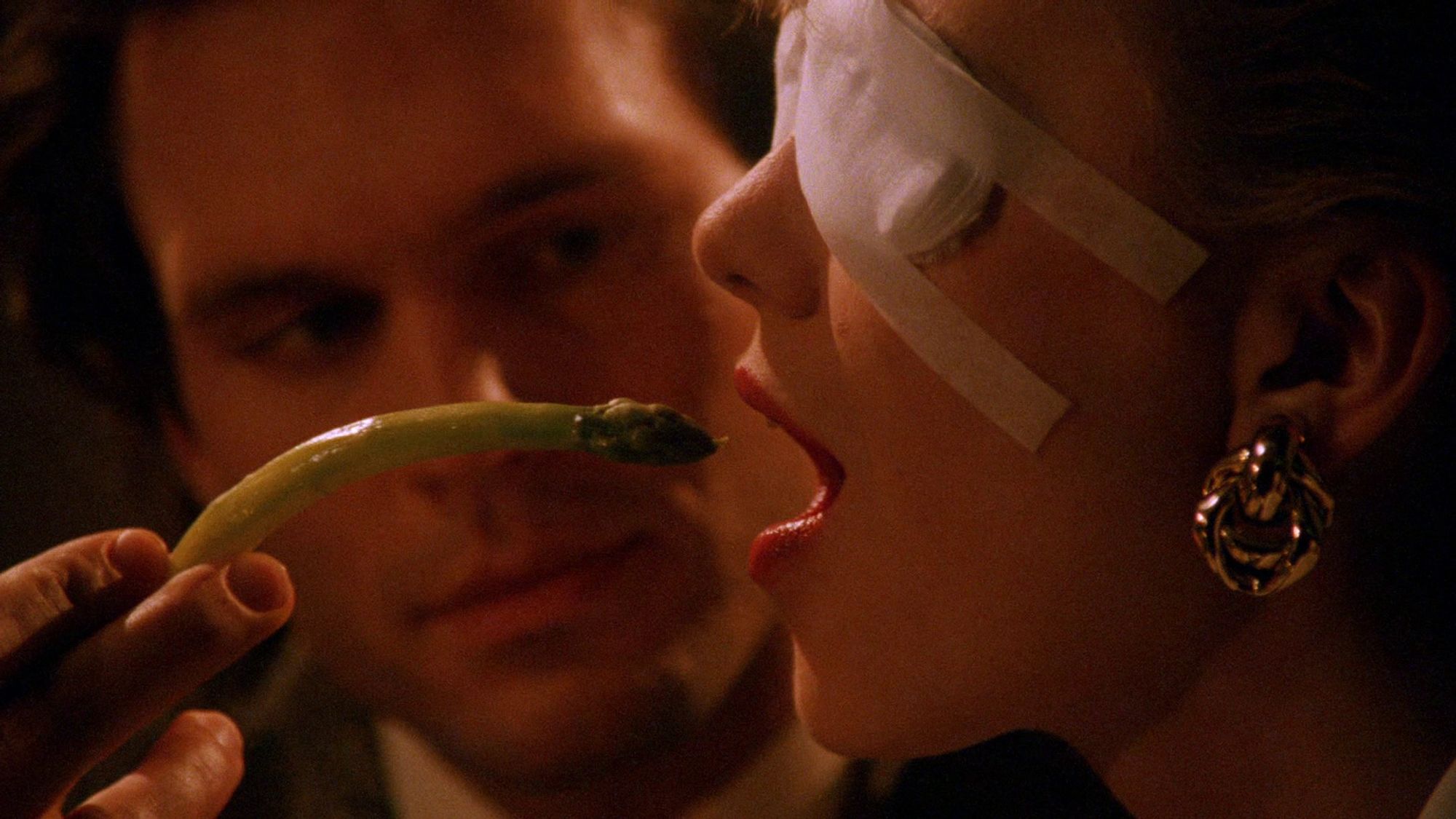 A man helpfully feeding a blind woman a single piece of asparagus.