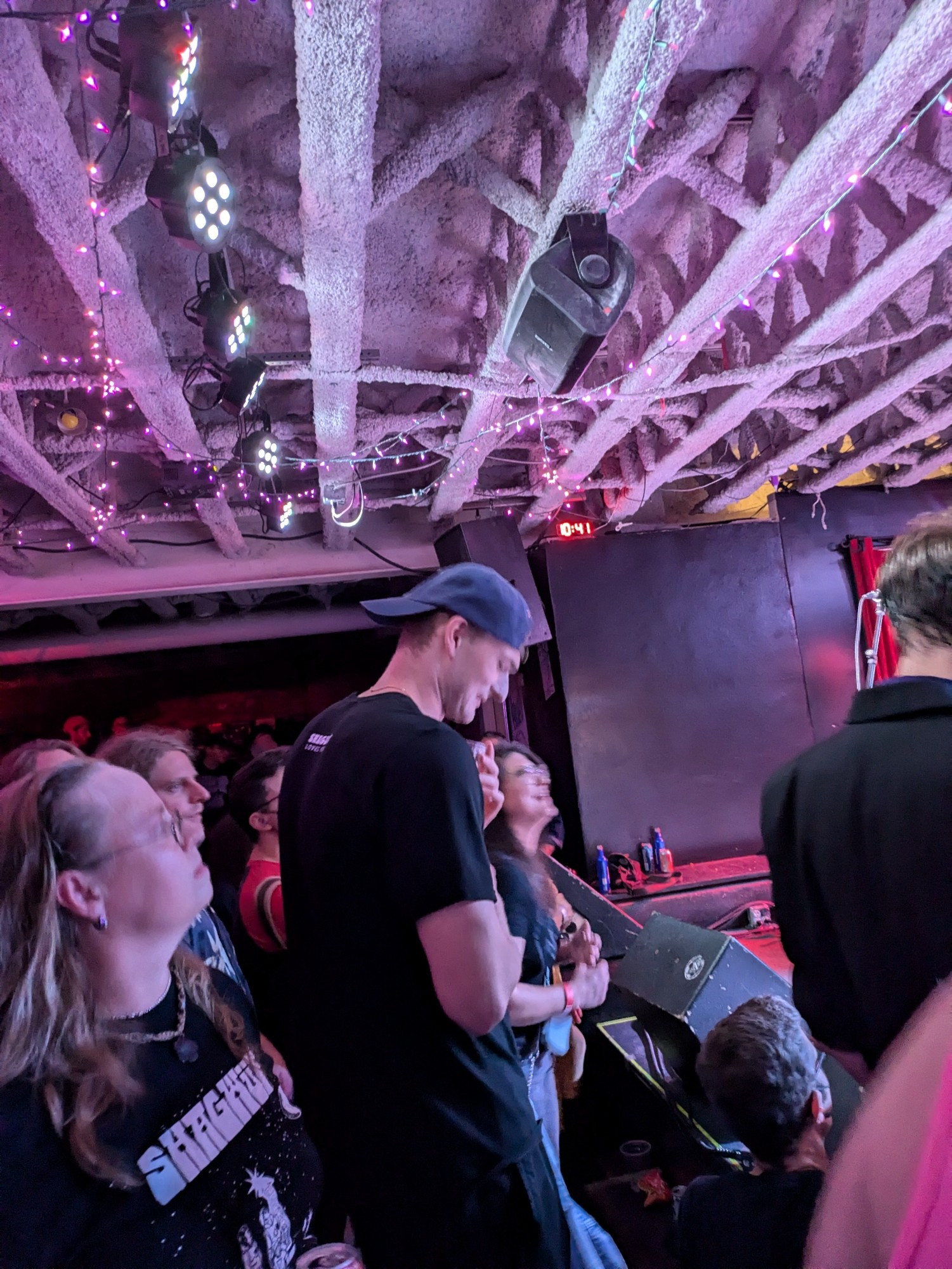 A very very tall man standing in the front row at a concert, blocking everybody's view behind him