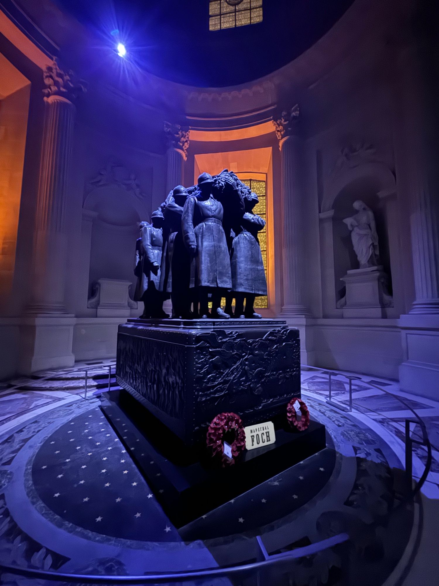 Thee angles of Foch’s tomb, in the dark but illuminated. It features bleak and anonymous figures of downtrodden looking poilus carrying his body